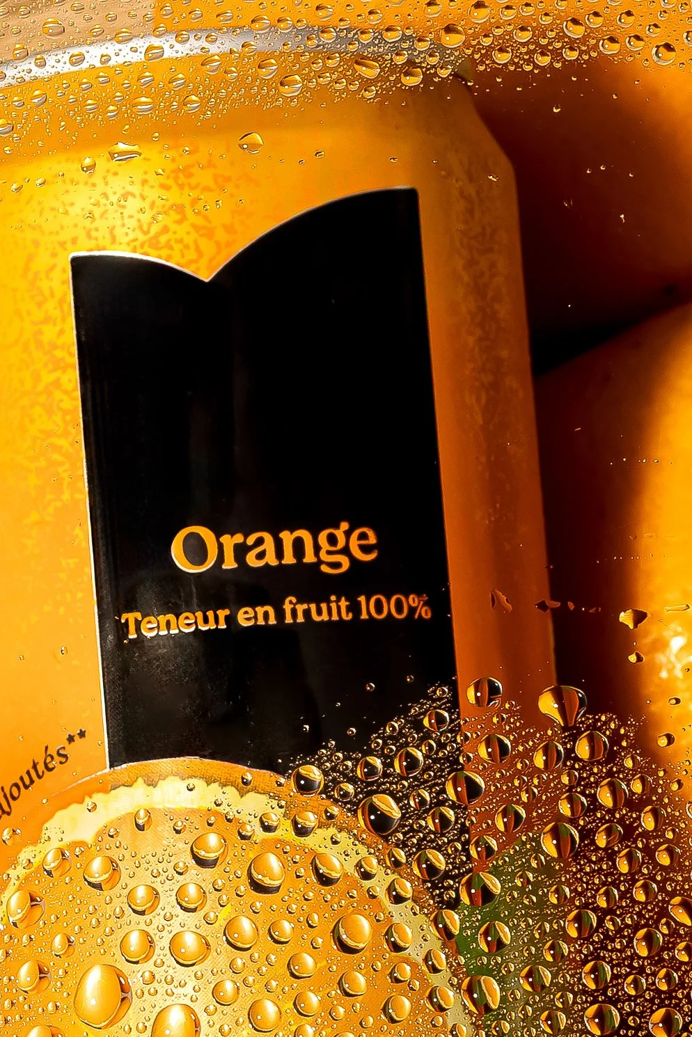 Gobelet en plastique contenant une boisson à l'orange, avec des gouttelettes d'eau sur la surface, et un fruit d'orange à côté.