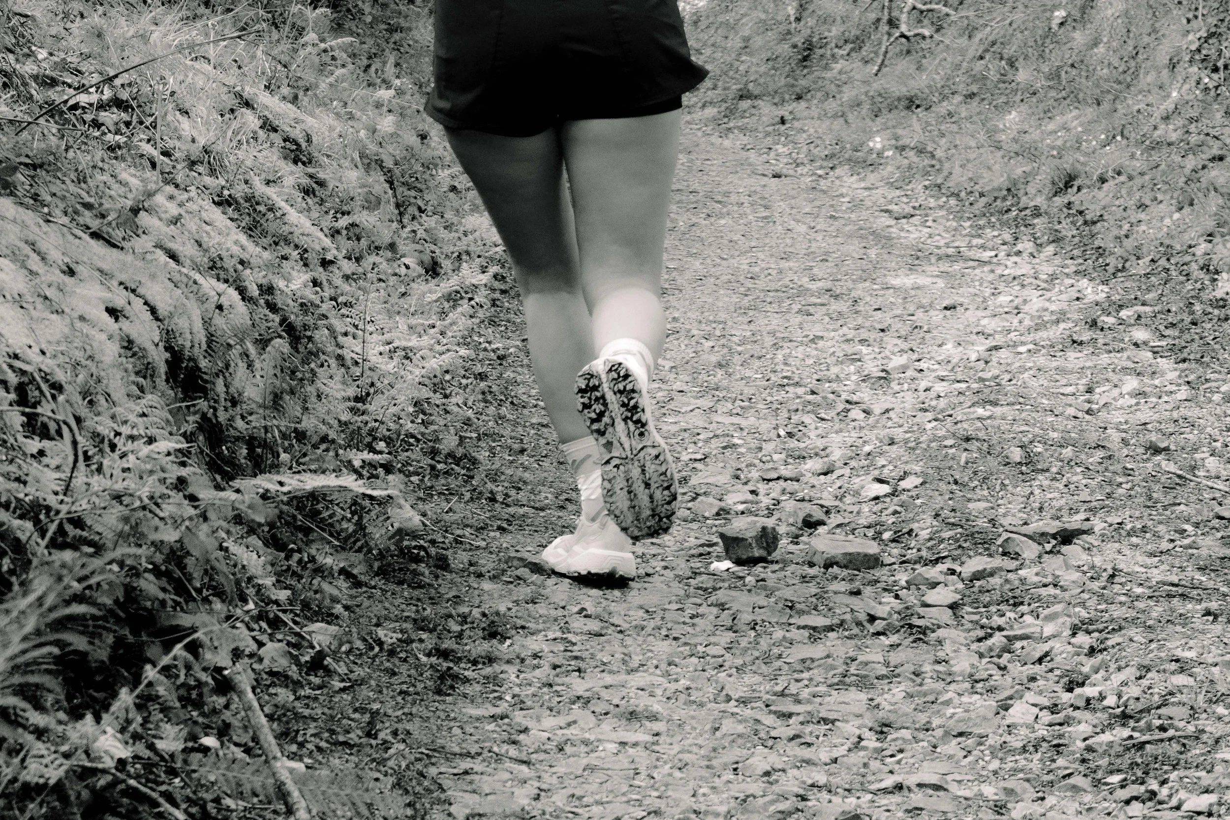 Personne en course ou marche à pied sur un sentier en nature, vue de derrière, portant des vêtements de sport et des chaussures de course.