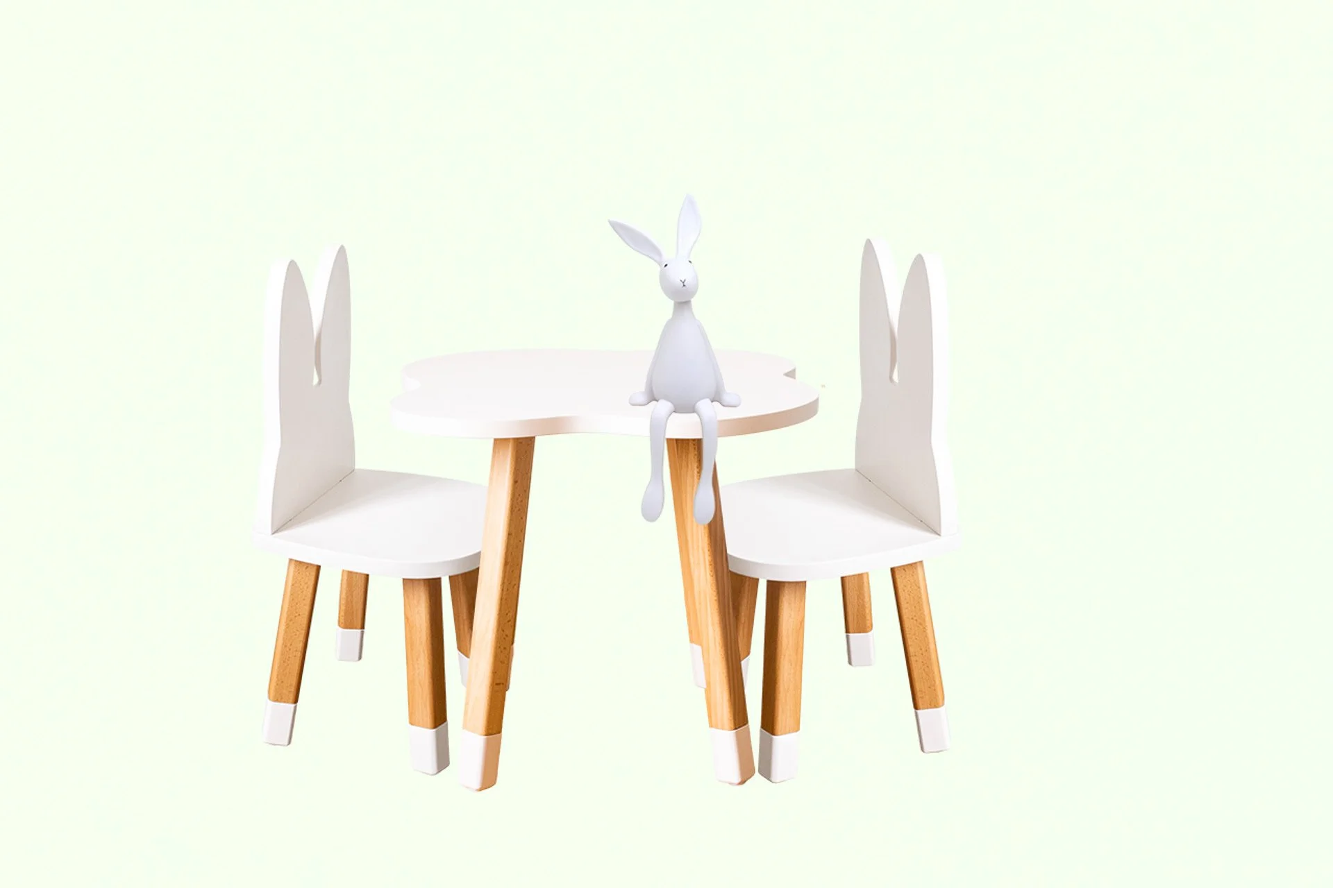 Petite table blanche avec deux chaises en bois et une figurine de lapin blanche assise au centre.
