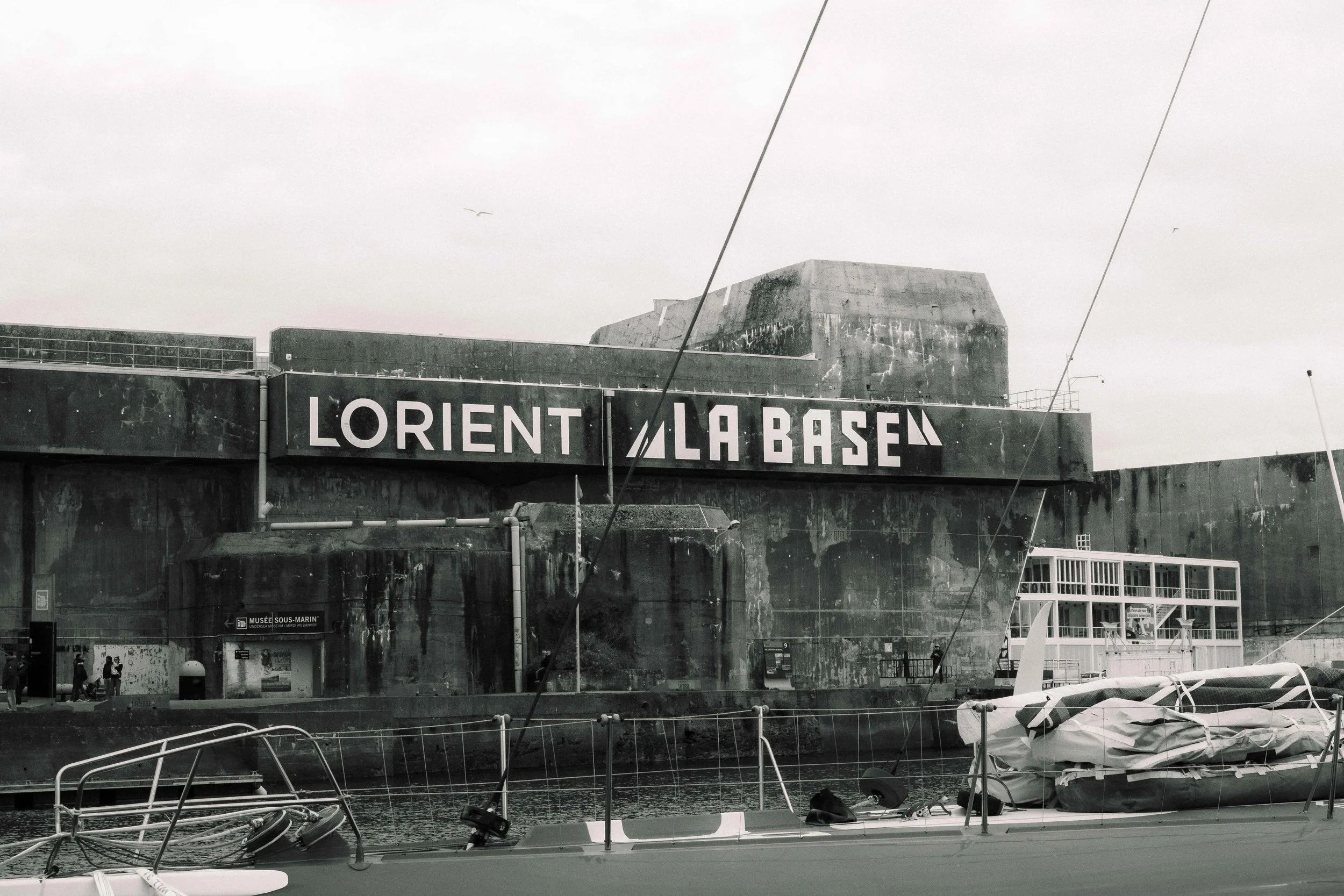 Vue du port de Lorient avec un bâtiment en arrière-plan portant le panneau 'Lorient La Base'.