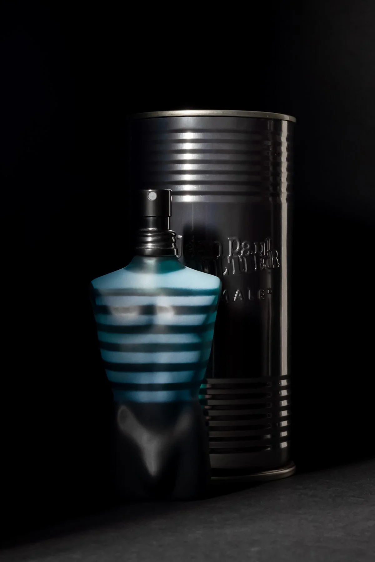 Flacon de parfum rayé bleu et blanc avec une bouteille noire à côté dans une boîte métallique noire