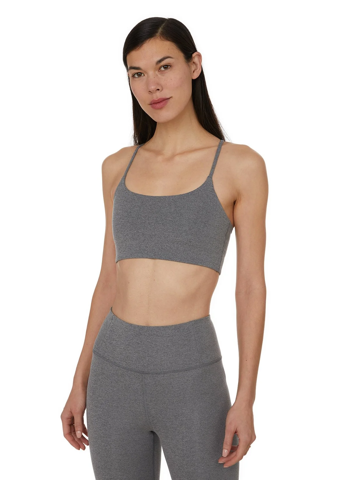 Une femme portant un haut de sport gris avec un pantalon de sport gris, debout contre un fond blanc.