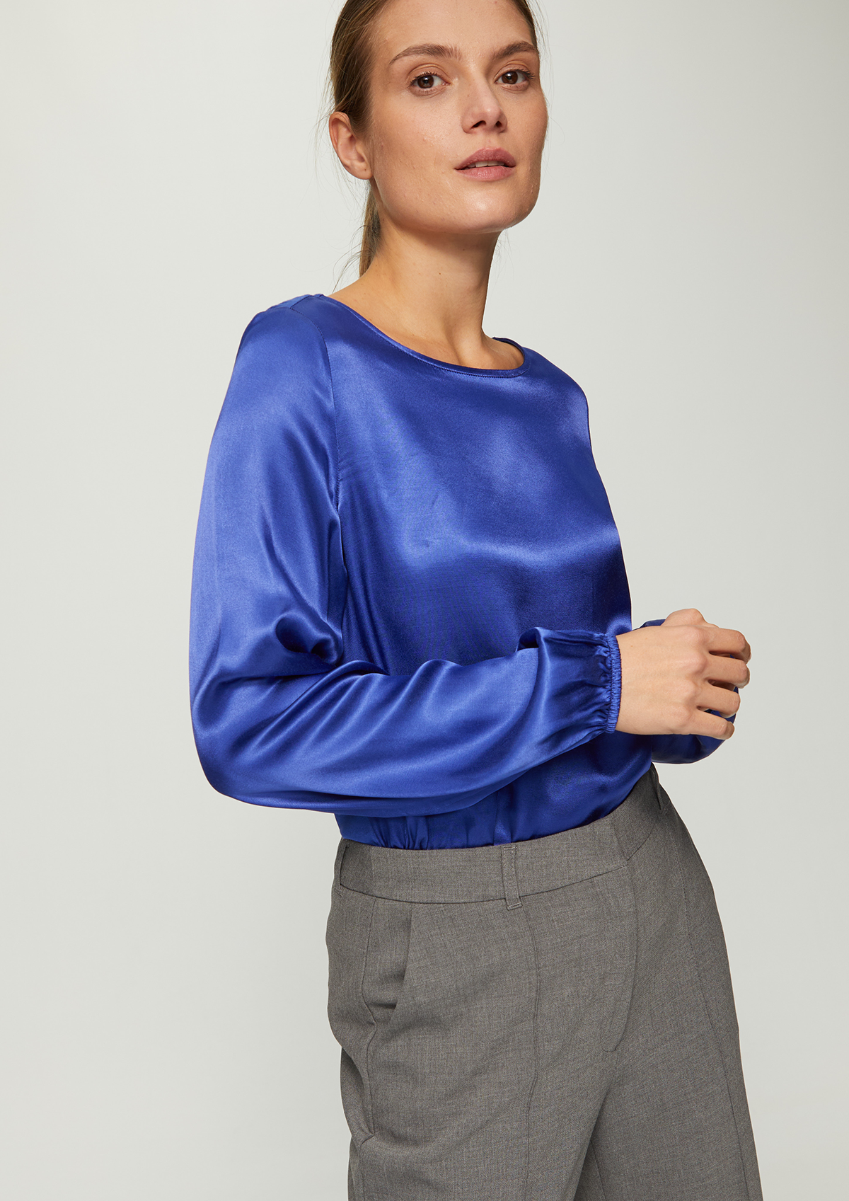 Femme portant un pull en satin bleu et un pantalon gris à motif à carreaux.