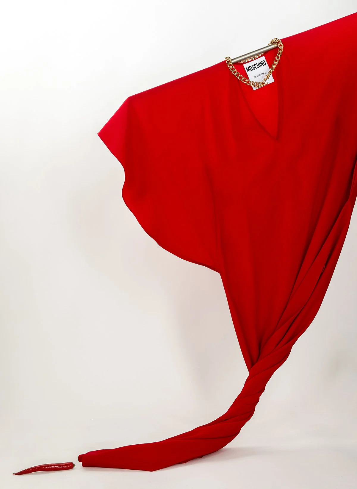 Robe rouge de haute couture suspendue avec une chaîne en or, polyester rouge s'étendant enroulée au sol, avec une étiquette 'MOSCHINO'
