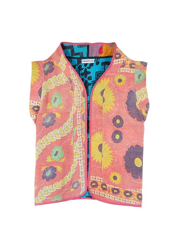 Gilet sans manches à motifs floraux jaunes, violets et verts sur fond rose, avec une doublure intérieure bleue aux motifs géométriques.