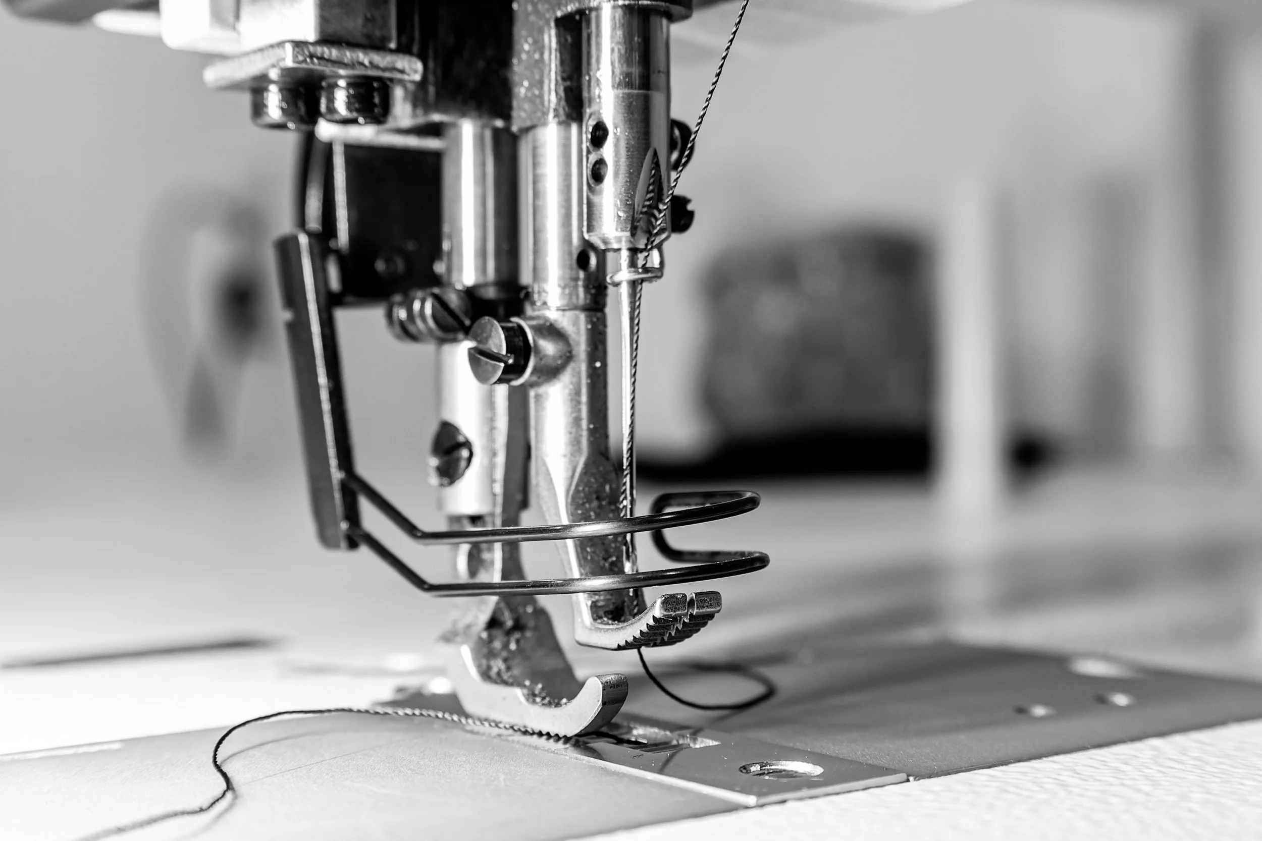 Une machine à coudre en noir et blanc, montrant la partie de la tête de la machine avec l'aiguille, le fil et la plaque à aiguilles.
