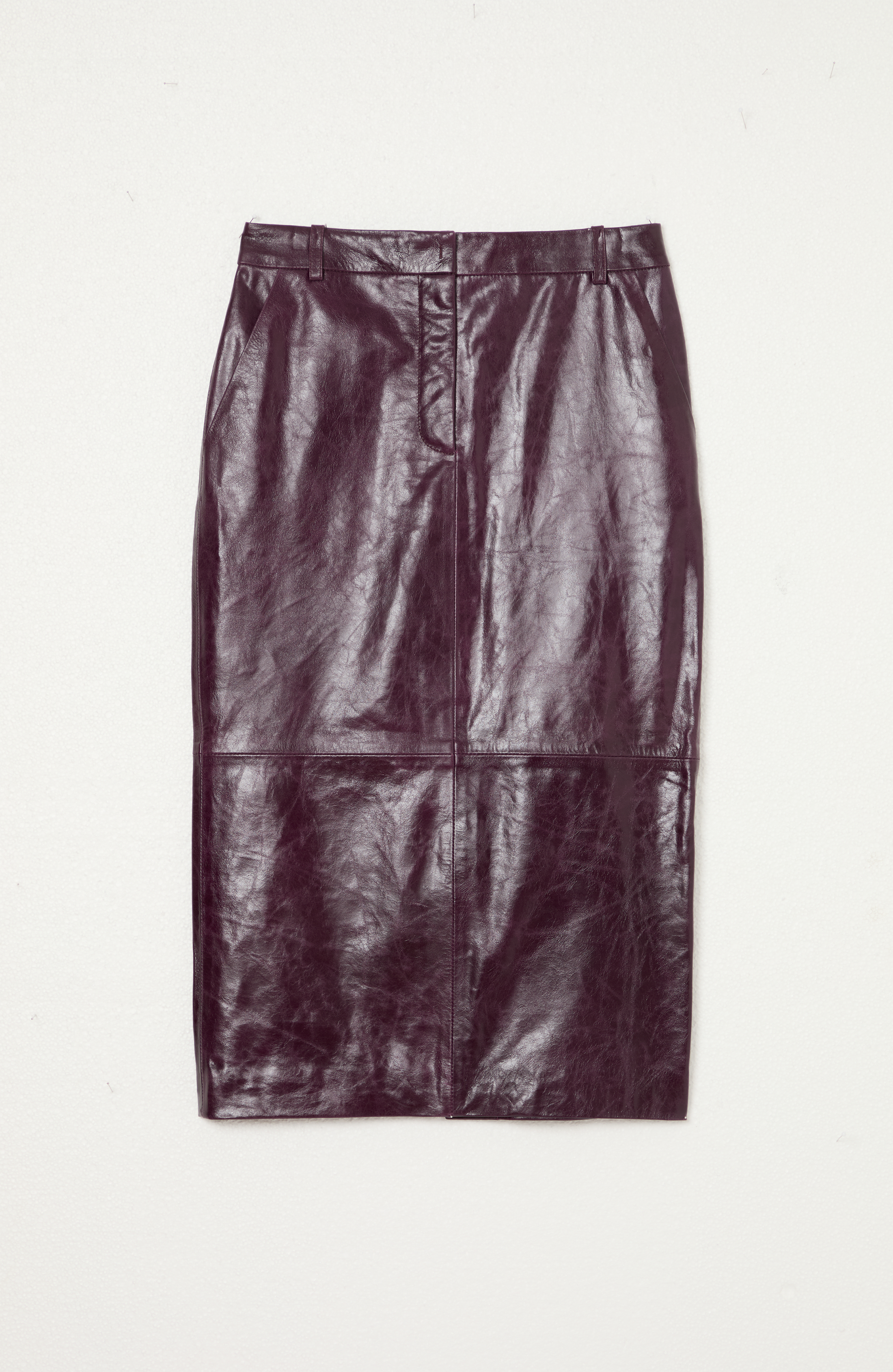 Jupe en cuir violet foncé suspendue contre un mur blanc.