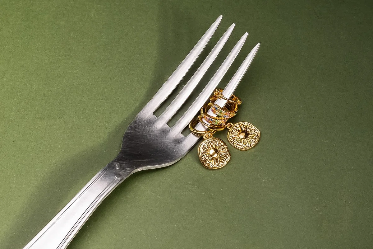 Une fourchette en métal argenté avec des boucles d'oreilles en or posées dessus, homme avec fond vert