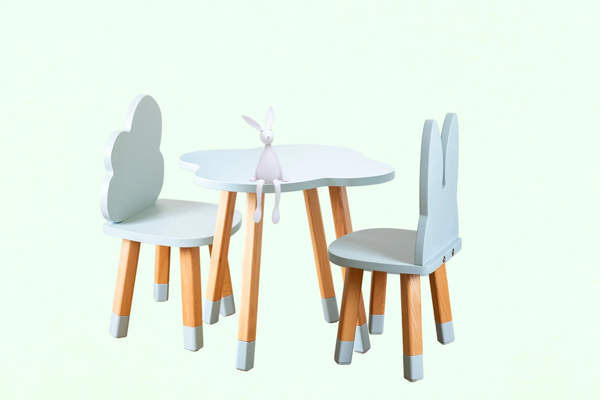 Un petit ensemble de mobilier pour enfant composé d'une table ronde blanche et de deux chaises en bois avec dossier en forme de lapin, et une figurine de lapin blanc suspendue au centre de la table.
