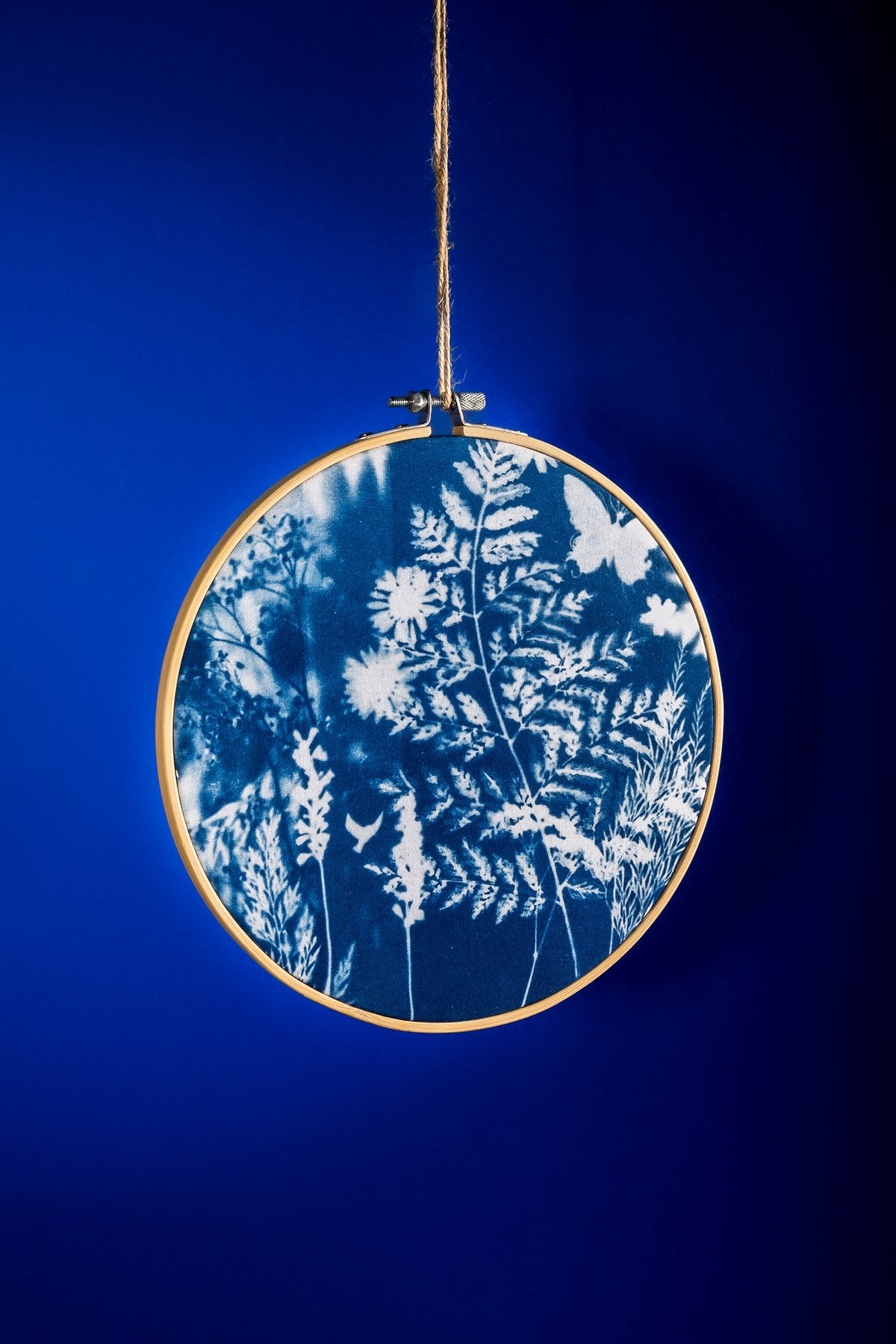 Une œuvre d'art suspendue représentant un motif de végétation en blanc sur un fond bleu, dans un cadre rond avec une suspension en corde.