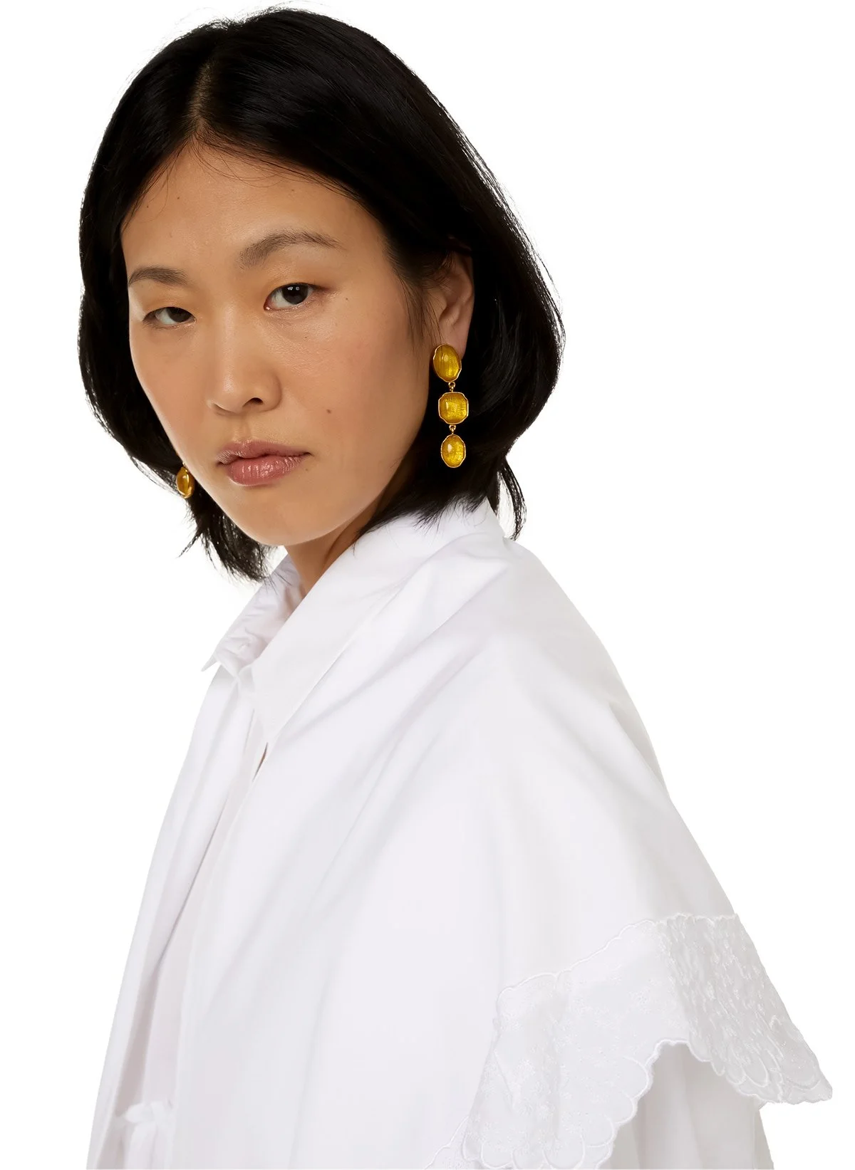 Portrait d'une femme asiatique avec de longs cheveux noirs, portant des boucles d'oreilles dorées et un chemisier blanc, regardant droit vers la caméra, sur fond blanc.