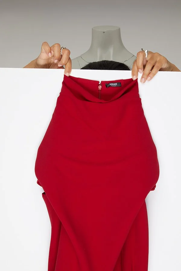 Une personne tient une jupe rouge devant un panneau blanc, avec un mannequin au centre.