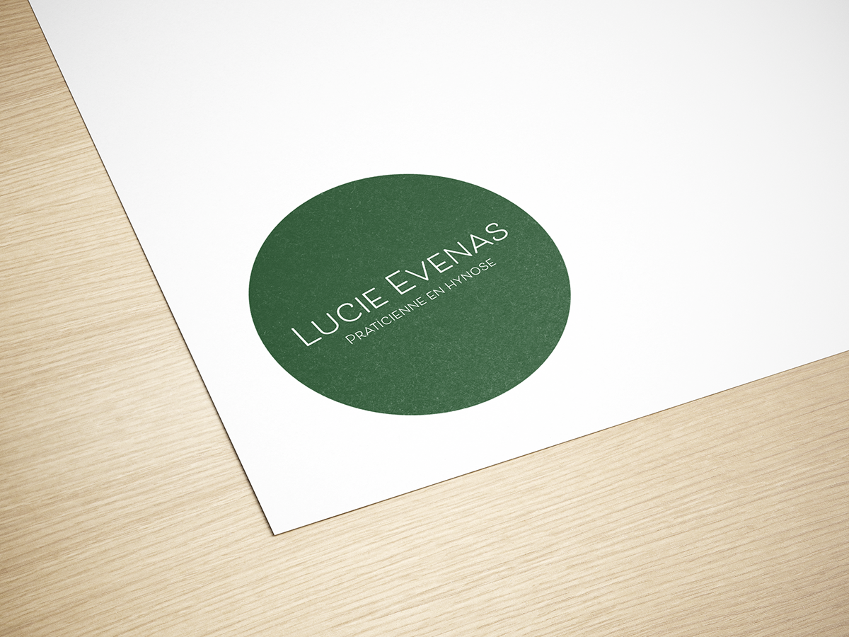 Carte de visite ou badge avec le nom Lucie Evenas, praticienne en hypnose, sur une surface en bois.