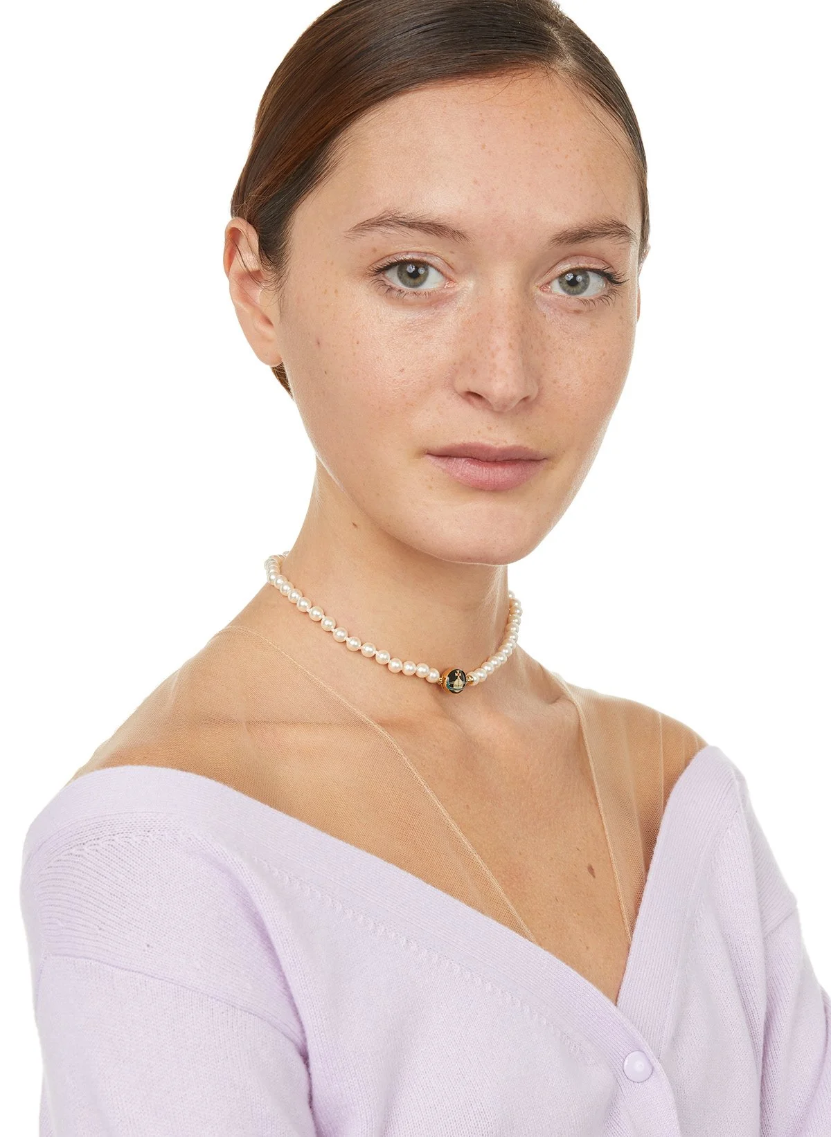 Jeune femme avec collier de perles, vêtue d'un haut rose clair à col en V, regardant devant elle.