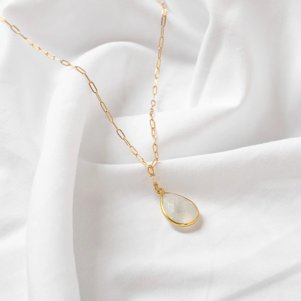 Collier en or avec pendentif en pierre translucide posée sur un tissu blanc