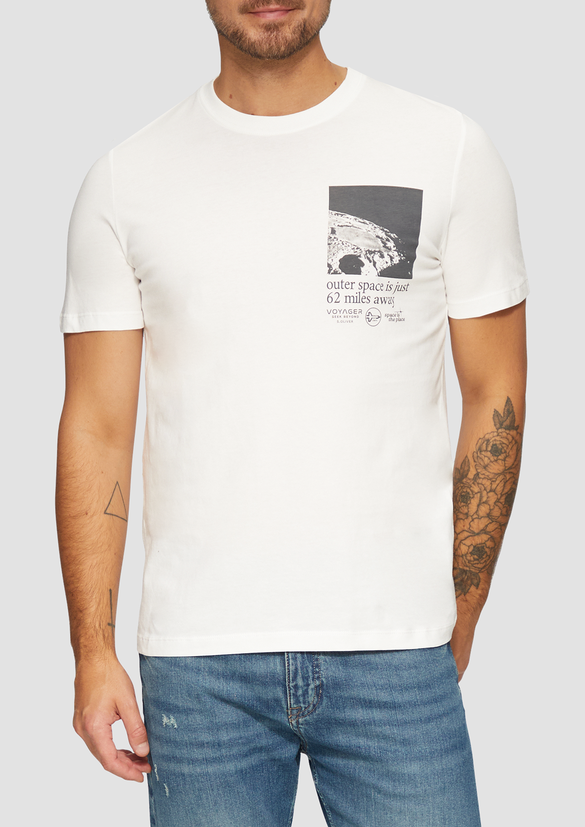 T-shirt blanc avec un graphique et un texte sur l'espace extérieur, porté par un homme avec tatouages, à côté d'un jean bleu.