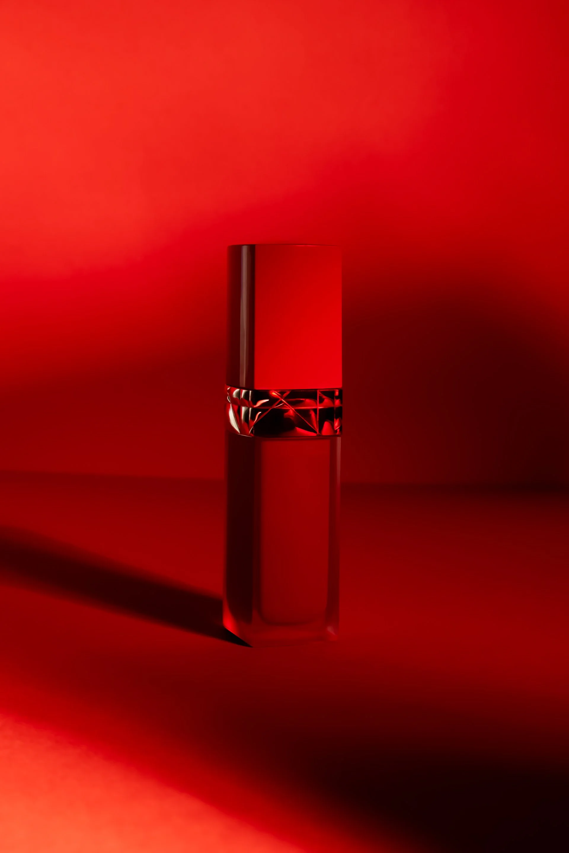 Un flacon de parfum rouge avec un design élégant, placé sur une surface rouge sous un éclairage tamisé.