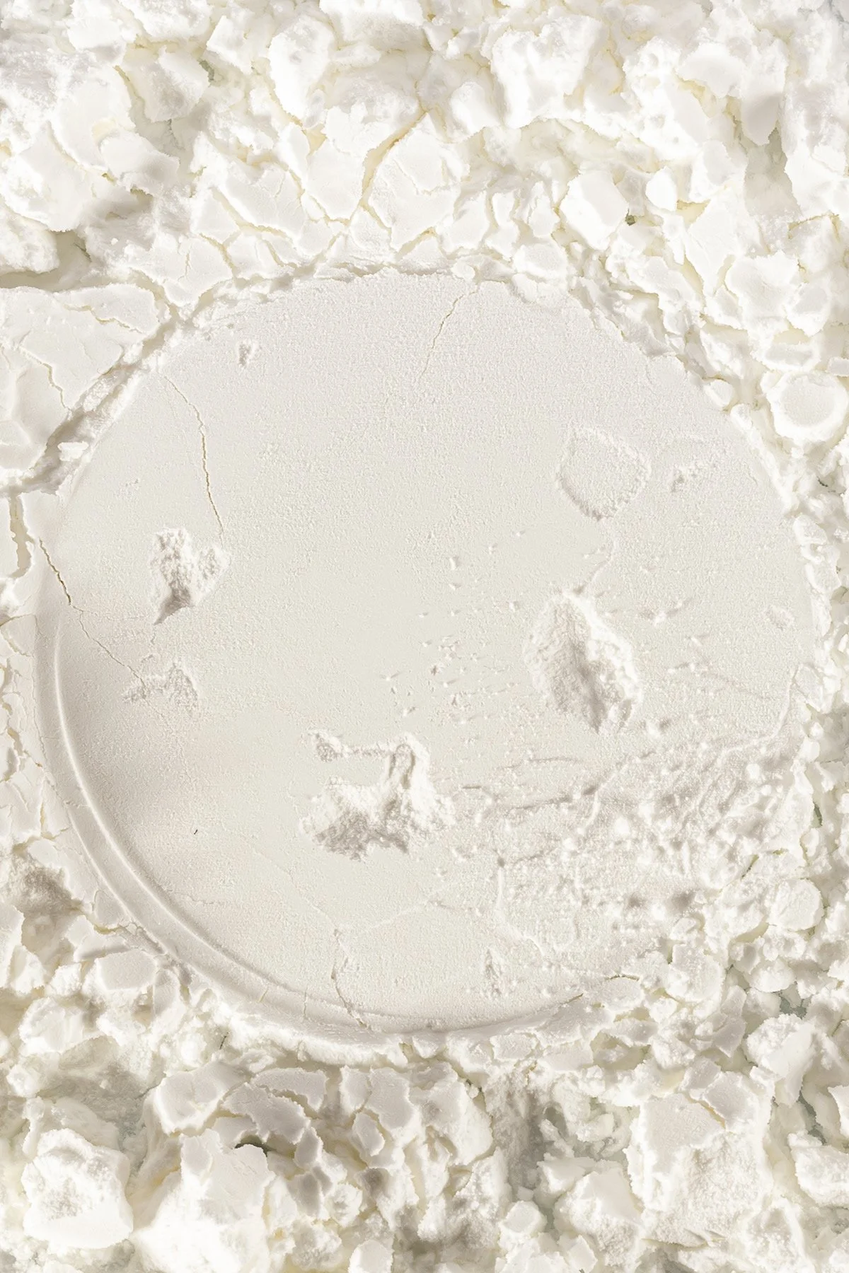 Poudre blanche de craie ou de farine disposée sur une surface, avec une zone centrale lisse et quelques morceaux éparpillés autour.