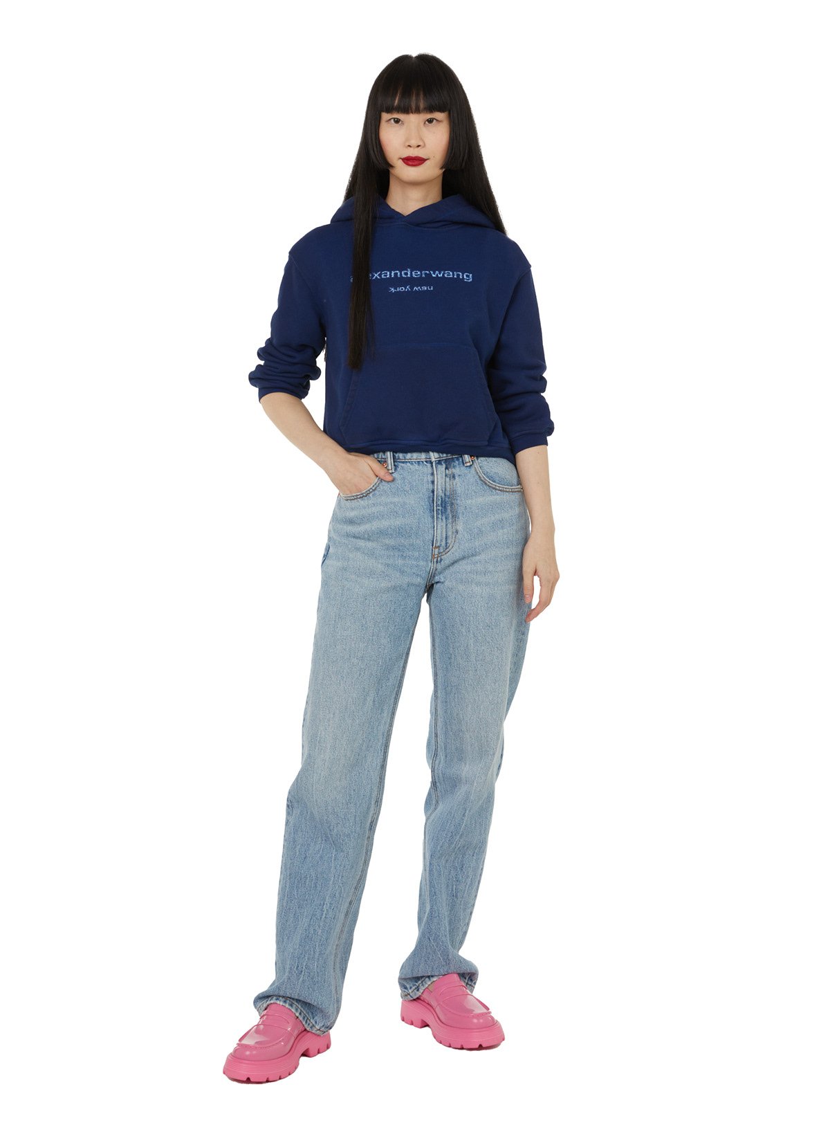 Jeune femme portant un sweat à capuche bleu, un jean délavé et des chaussures roses.