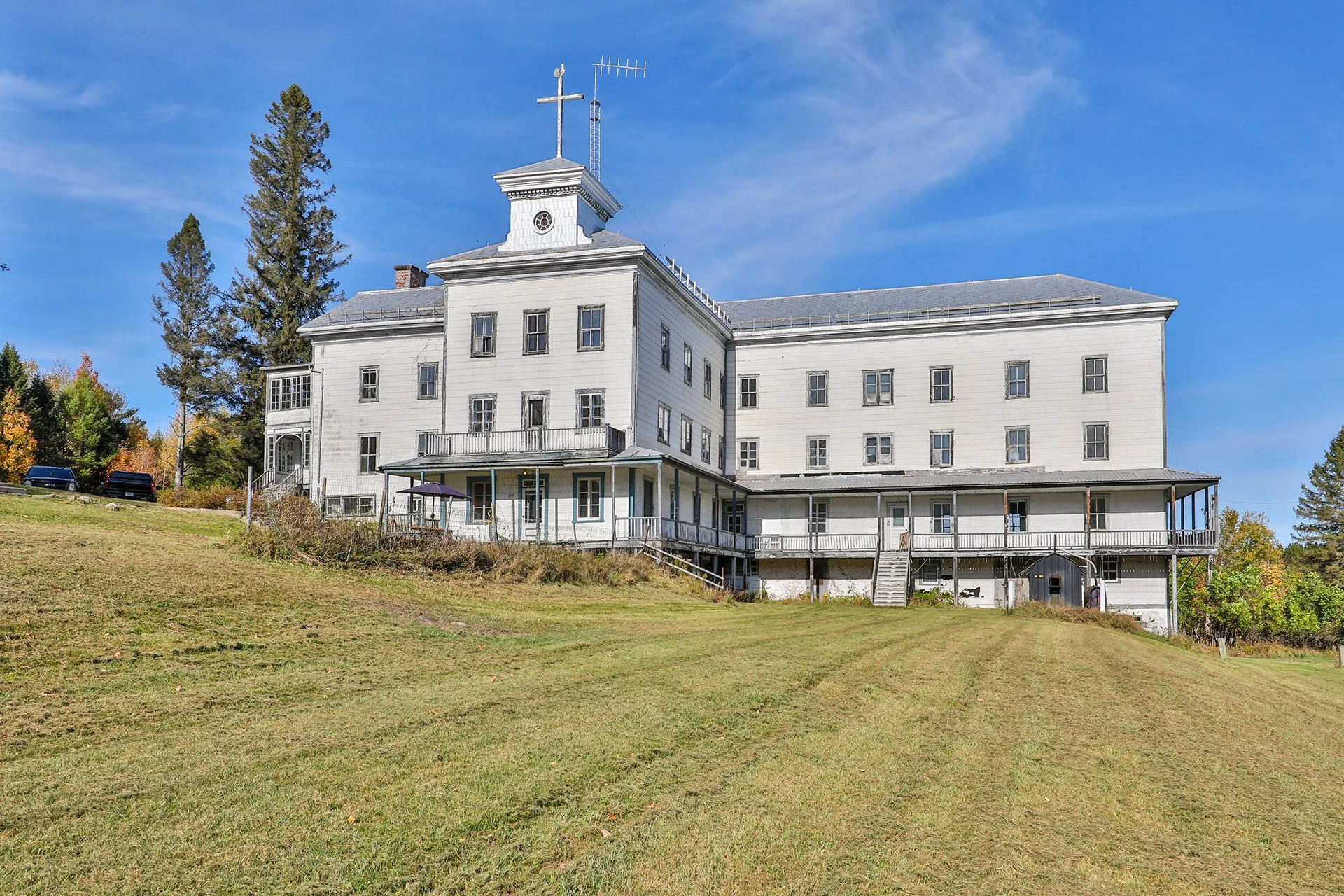 Grand bâtiment blanc en style victorien avec un clocher, située dans un paysage verdoyant avec un ciel bleu clair.