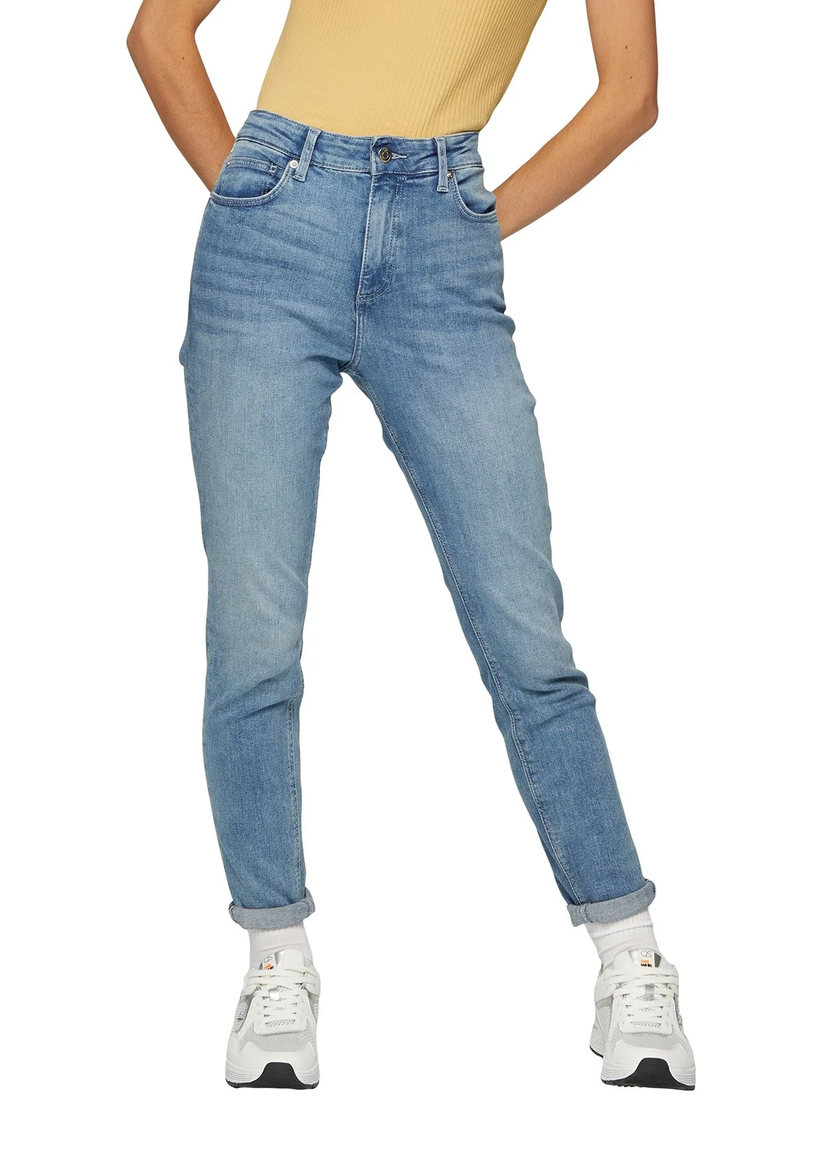 Jeune femme portant un haut jaune, un jean bleu clair, des chaussettes blanches et des baskets blanches, vue de la taille aux pieds.