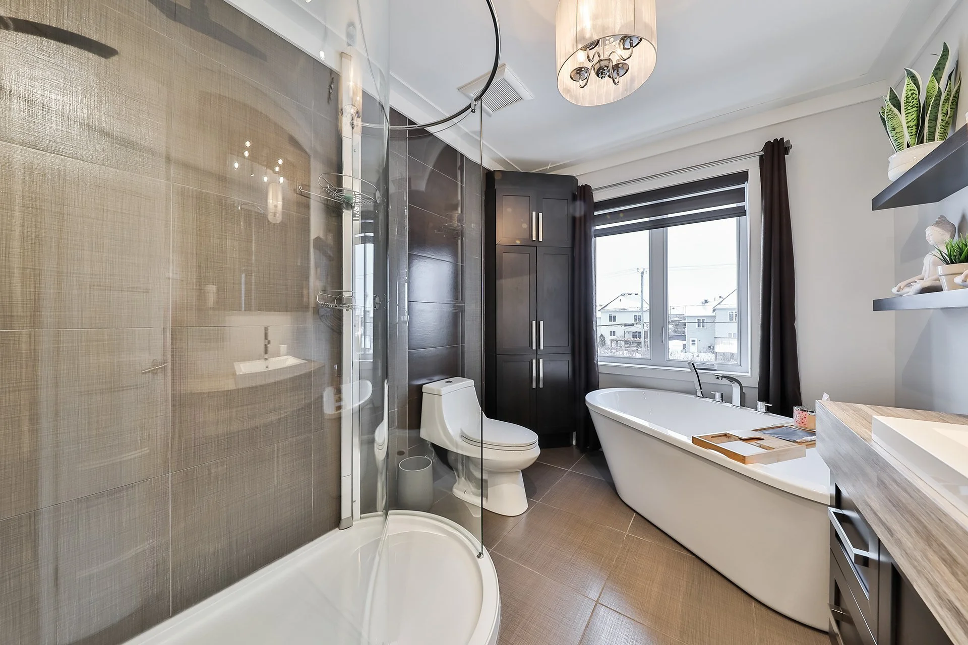 Salle de bain moderne avec douche, toilette, baignoire, grand fenêtre, étagères décoratives et meubles sombres