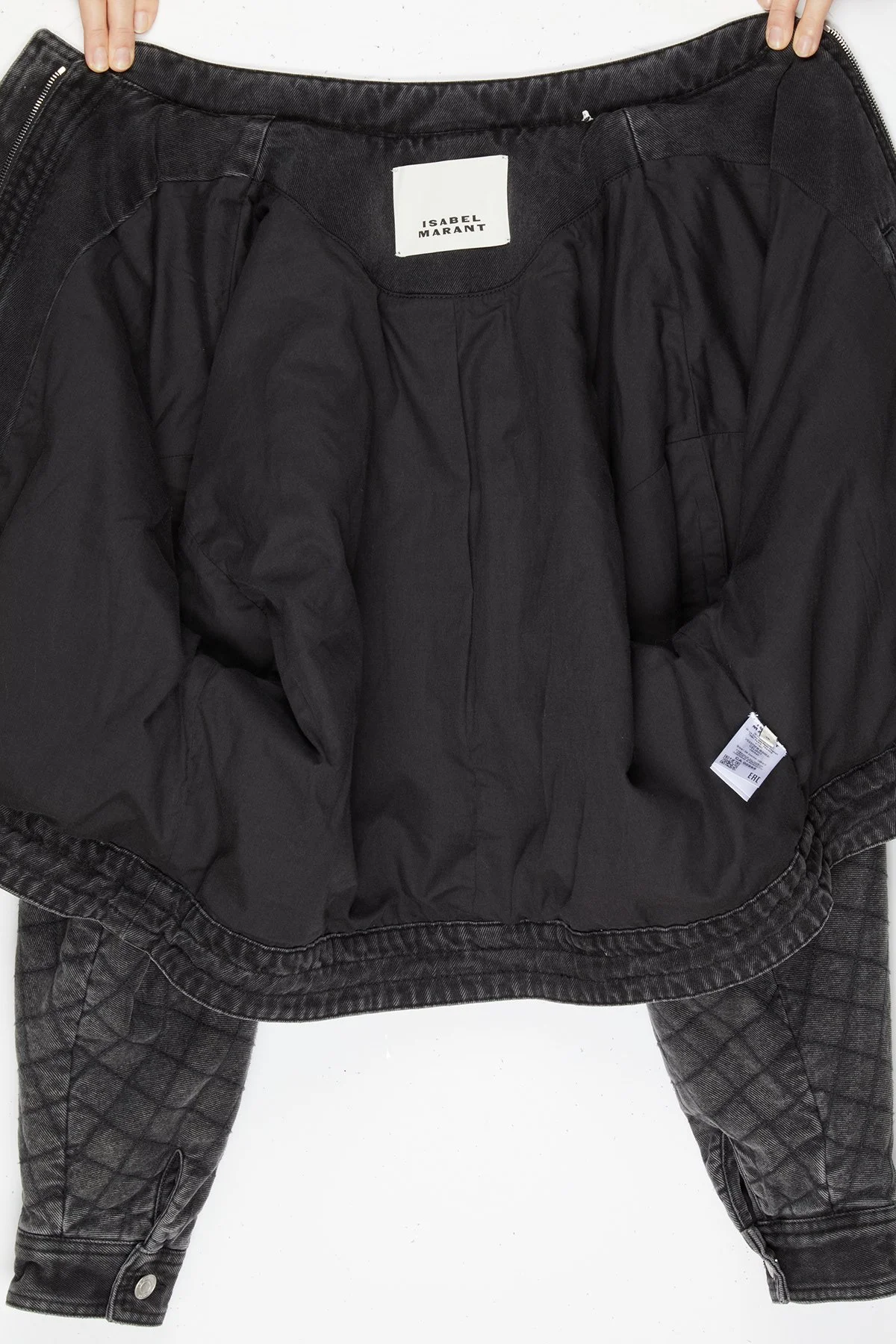 Veste noire ouverte pour montrer l'intérieur, avec un label blanc 'Isabel Marant' et un jean gris à motif.