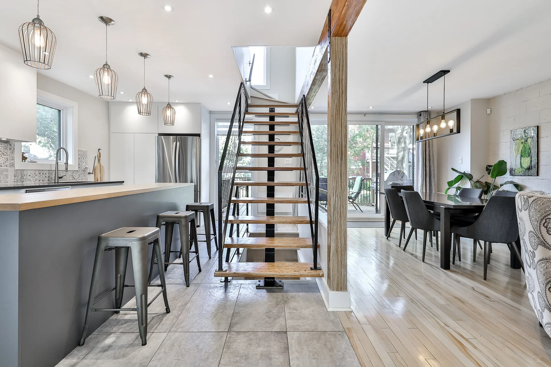 Intérieur moderne d'une maison avec cuisine, salle à manger et escalier en bois avec structure en métal.
