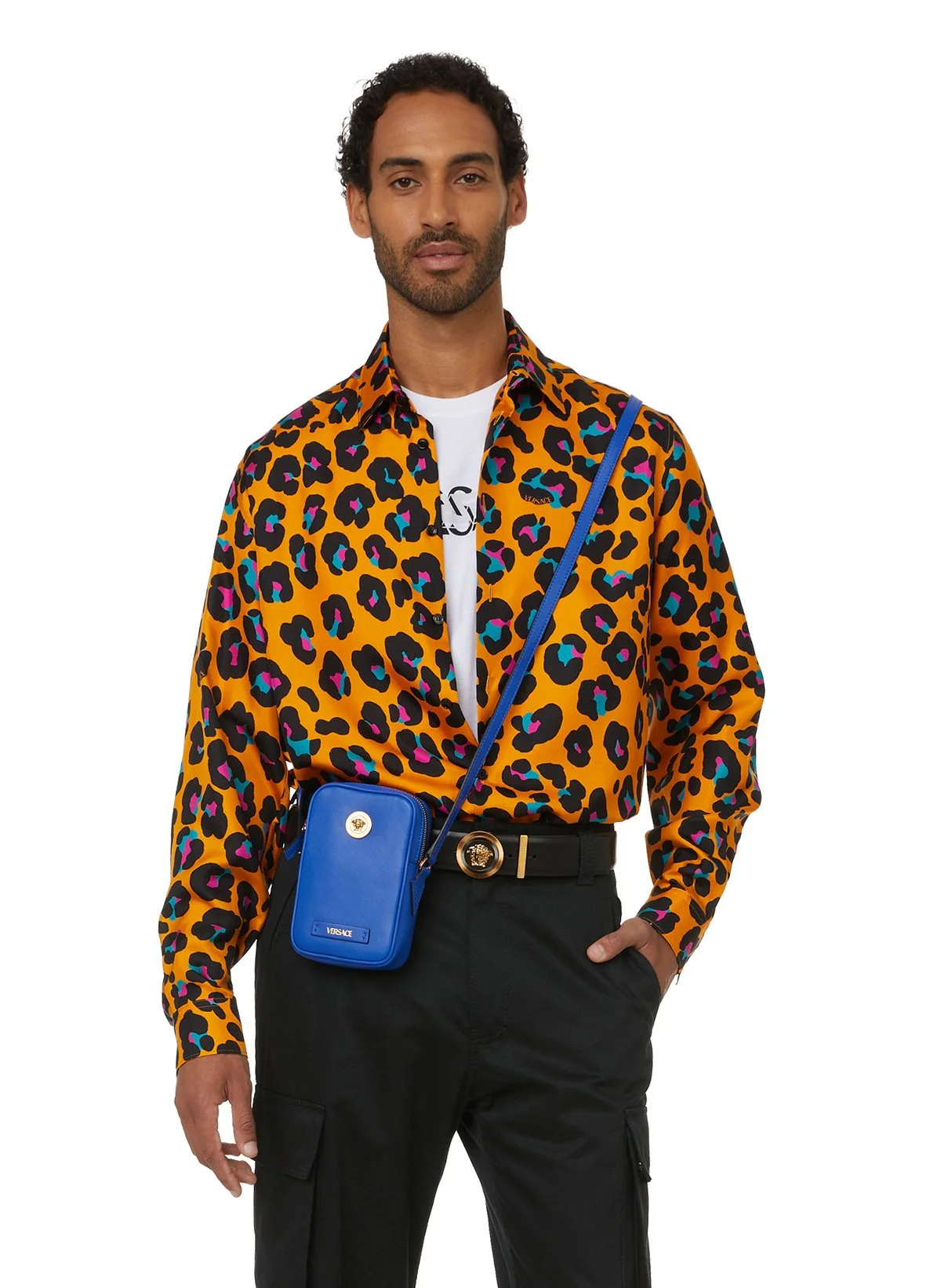 Homme portant une chemise à motifs léopard orange, un sac à bandoulière bleu de la marque Versace, et un pantalon noir.
