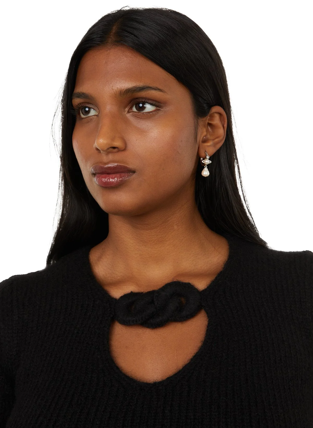Portrait d'une femme avec des cheveux noirs, portant des boucles d'oreilles perle et un pull noir avec un détail en forme de nœud au niveau du col