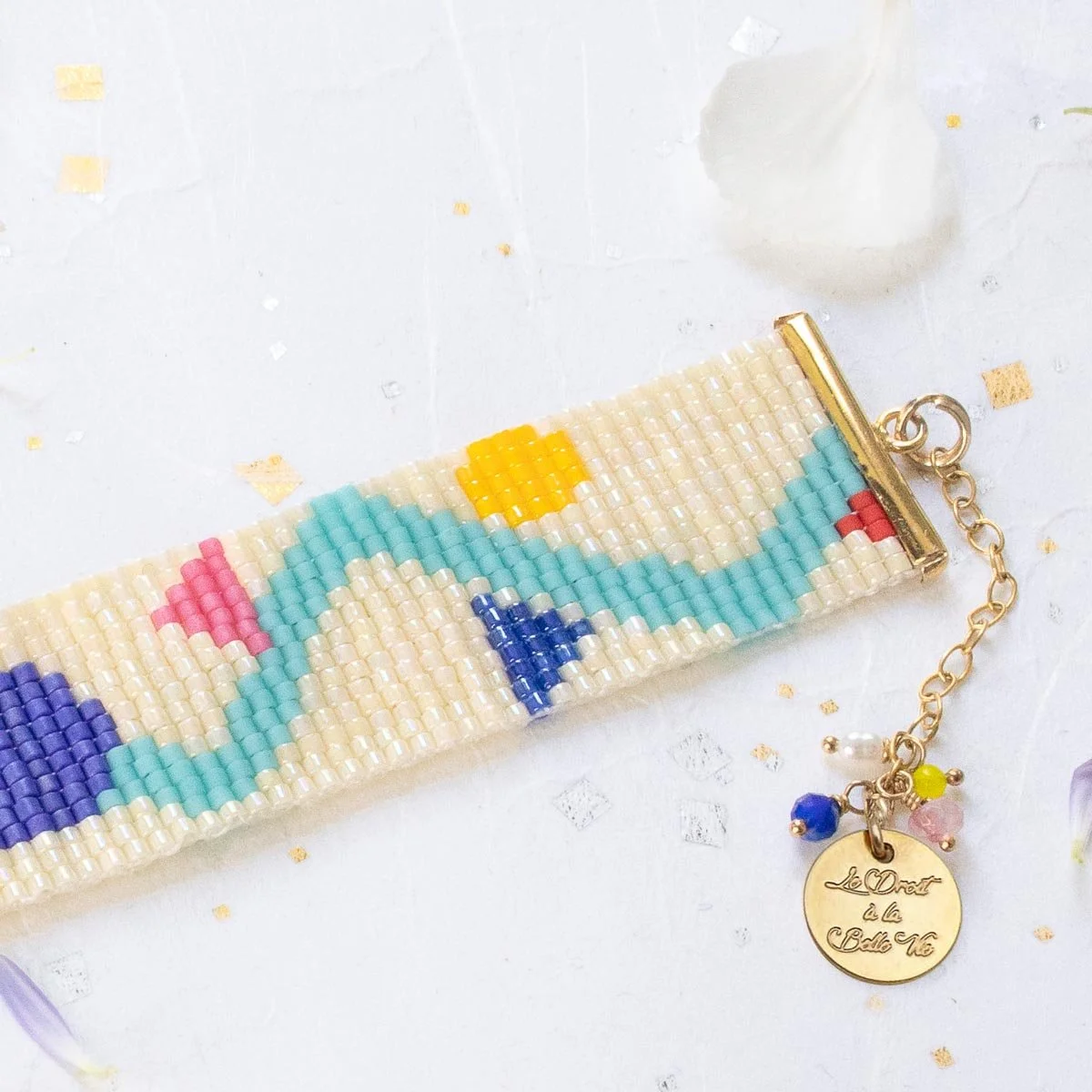 Bracelet en perles colorées avec un motif printanier, attaché à une chaîne dorée avec un pendentif gravé.