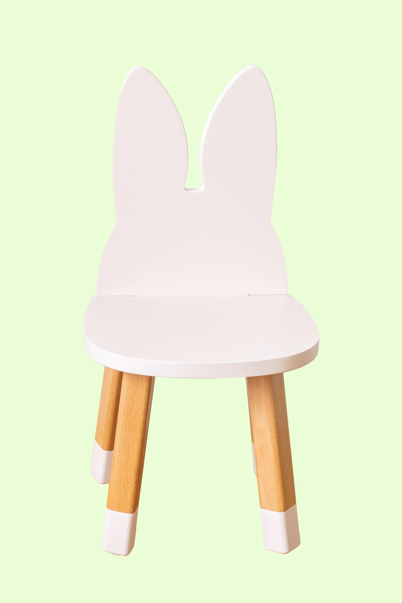 Chaise en blanc avec dossier en forme de lapin et pieds en bois, fond vert clair.