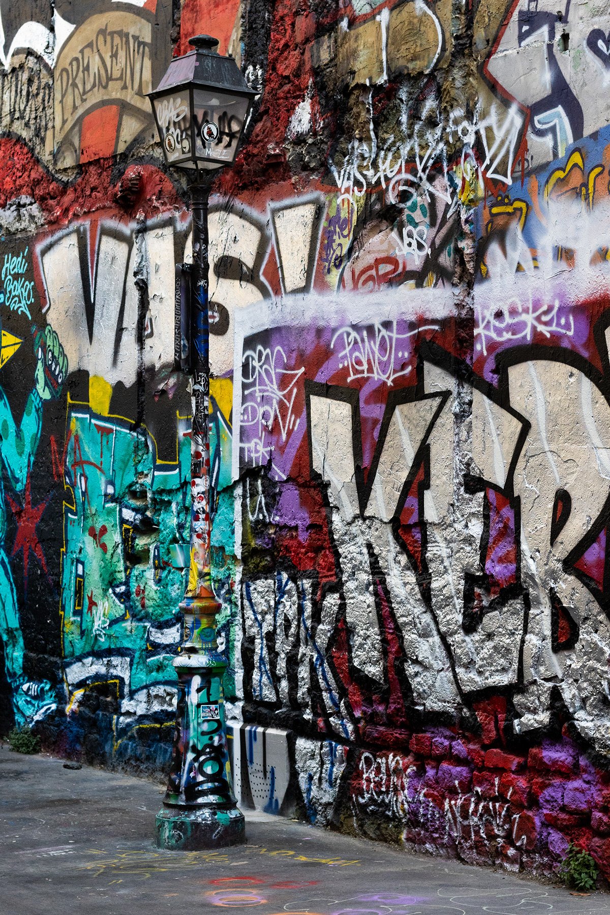 Un mur recouvert de graffiti coloré avec une vieille lanterne de rue noire devant lui, tachée de peinture graffiti.