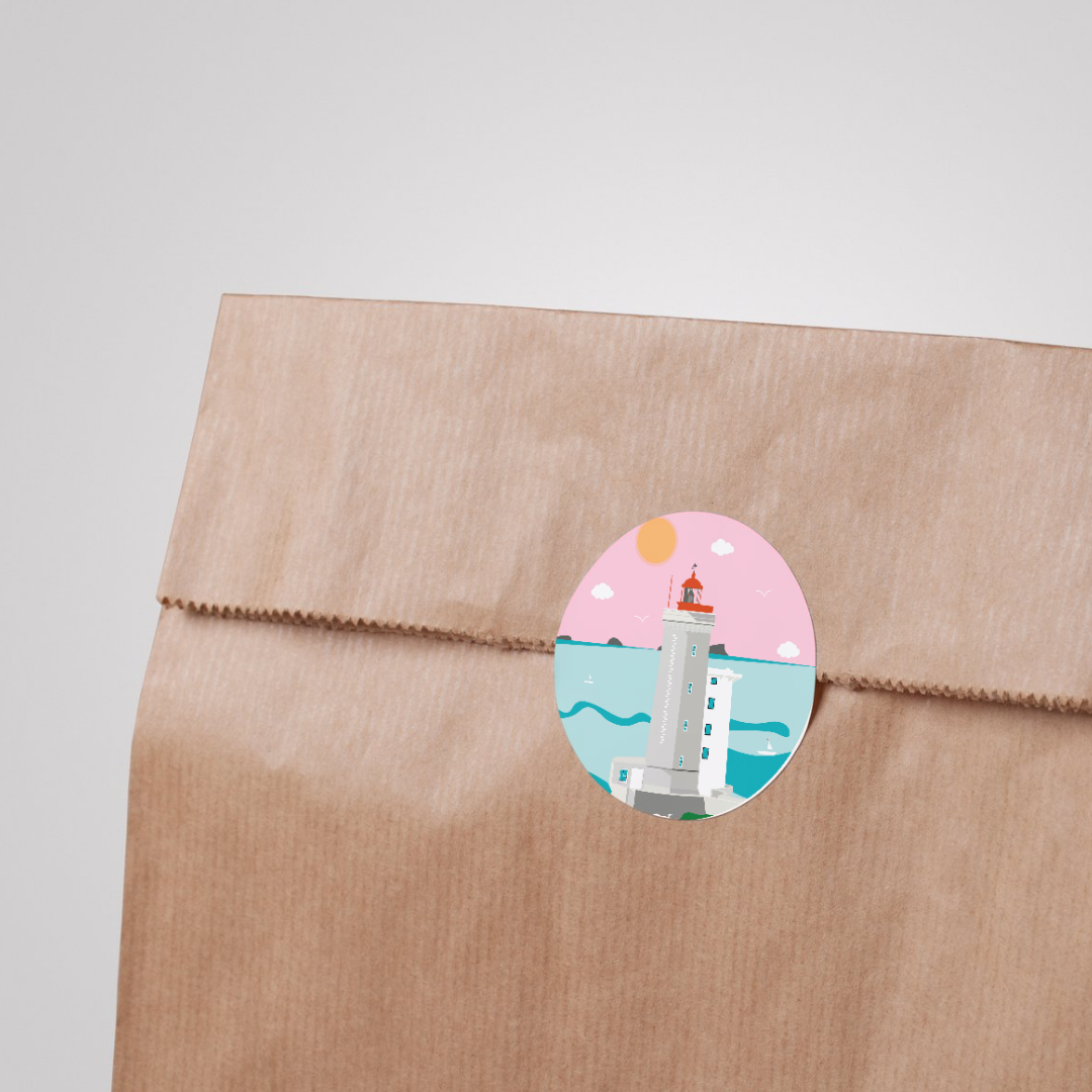 Un sac en papier kraft avec un sticker illustré d'un phare en bord de mer sous un ciel rose, avec un soleil orange et quelques nuages.