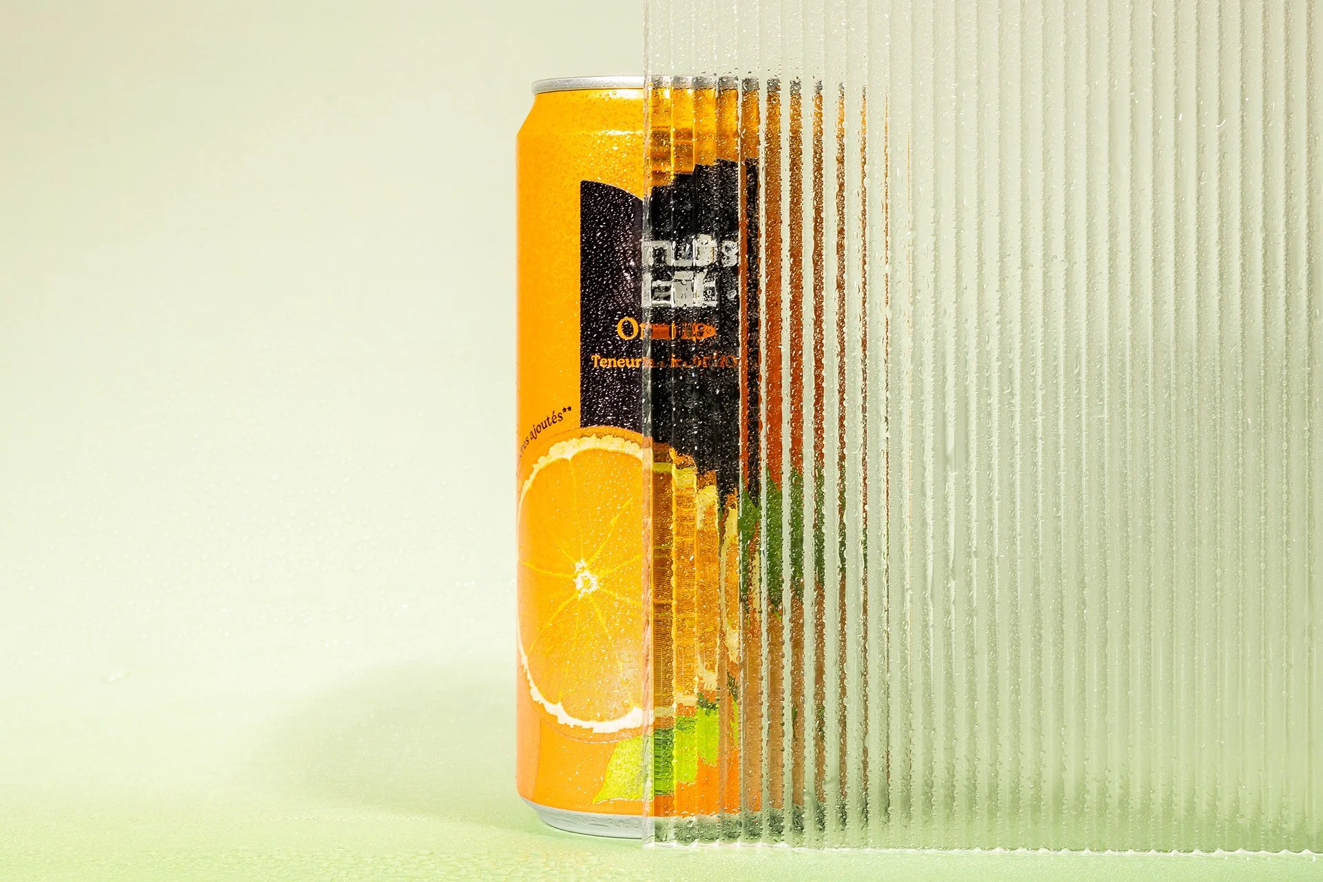 Une canette orange avec un motif d'orange tranchée et de feuilles, à moitié à travers une surface en verre striée.