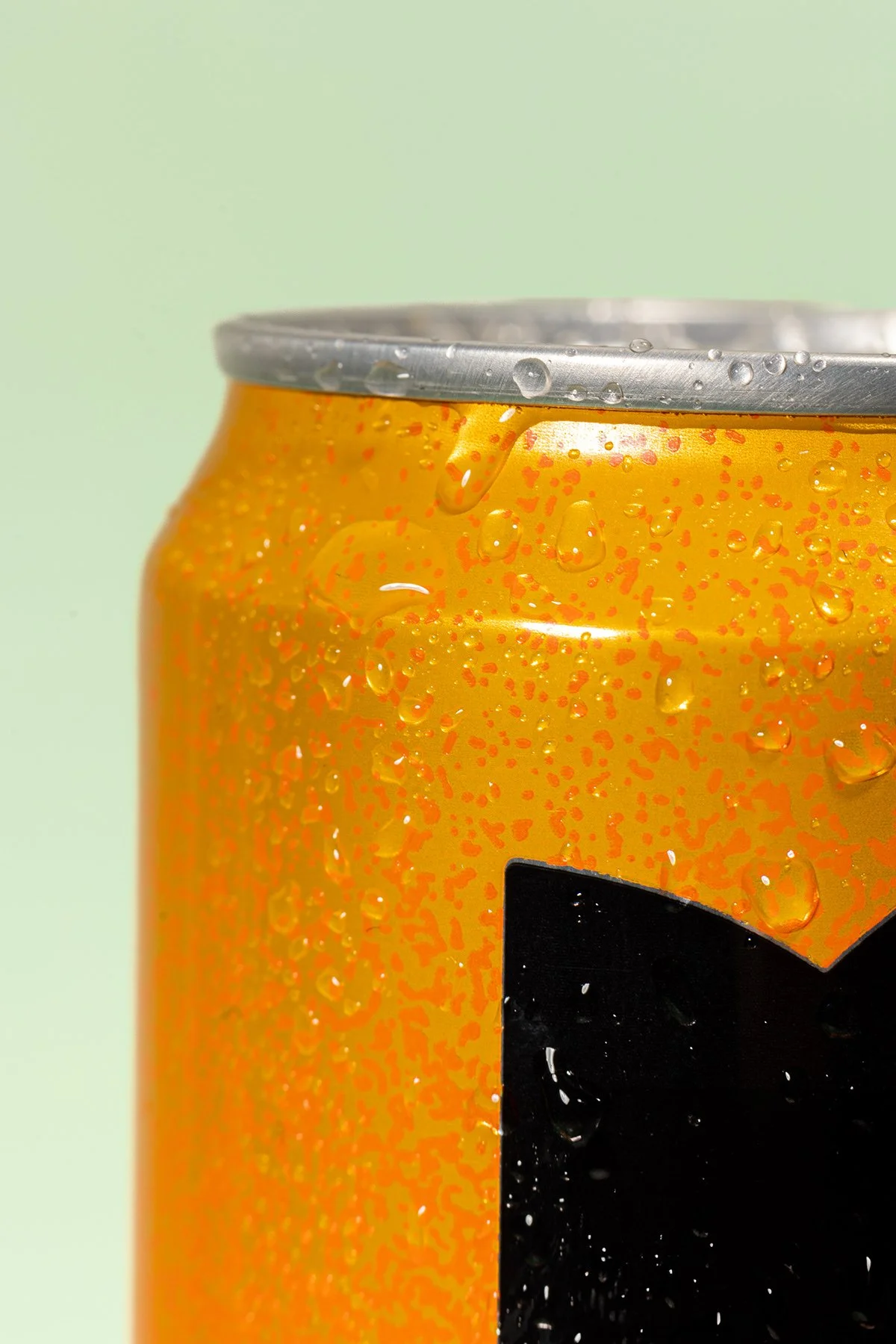 Canette de soda orange fraîche avec des gouttelettes d'eau sur la surface, visible partie d'une étiquette noire avec un logo en forme de sourire noir, fond en dégradé clair