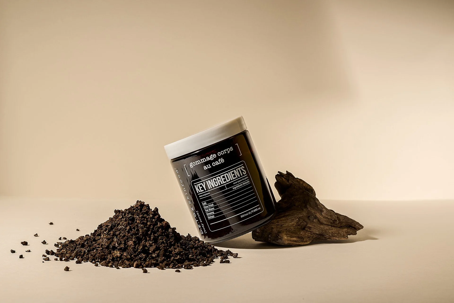 Pot de gommage corporel au café posé sur un morceau de bois avec du café moulu devant.