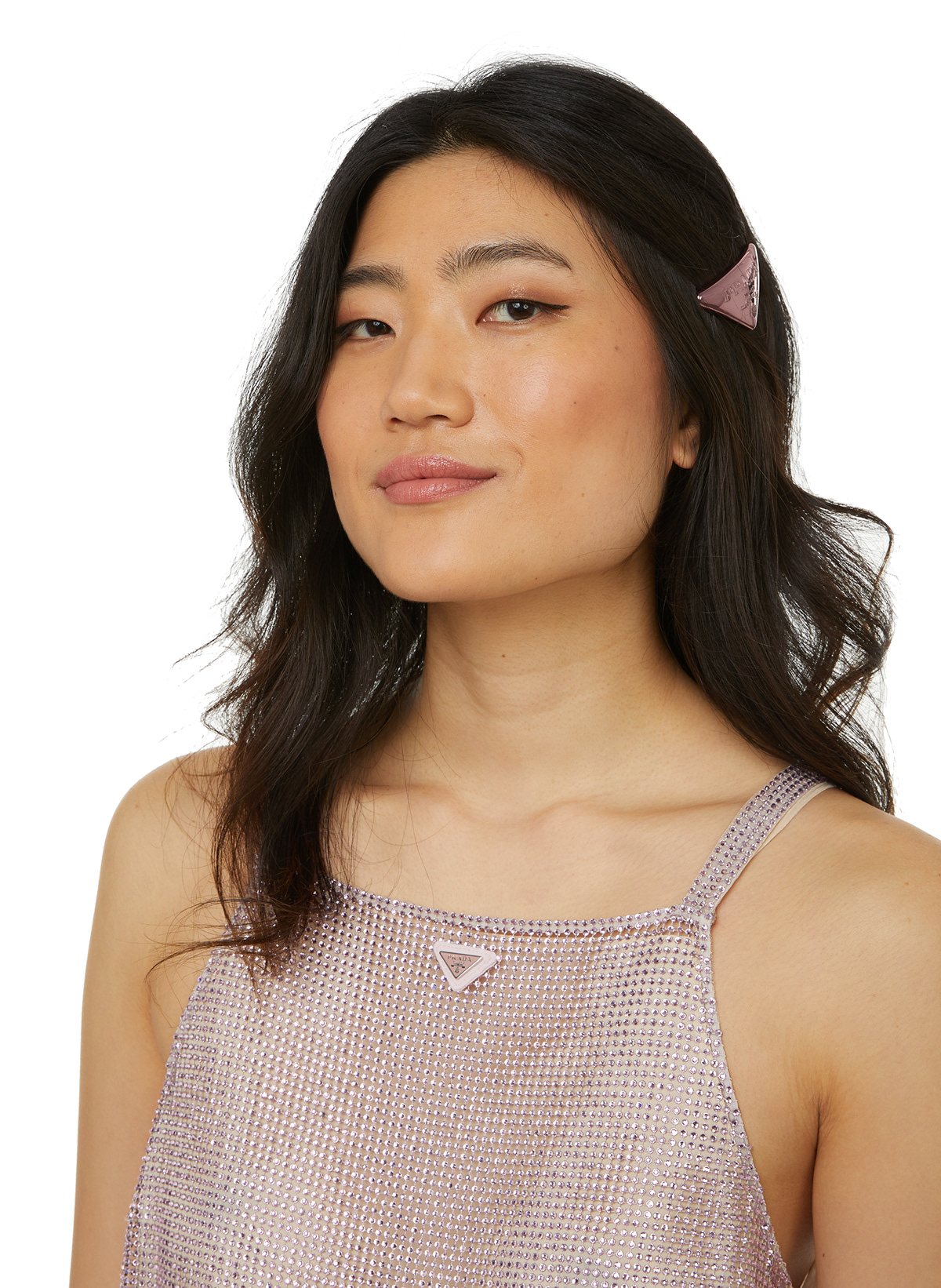 Une femme avec des cheveux longs et ondulés portant un haut brillant avec des bretelles et une épingle à cheveux violette.