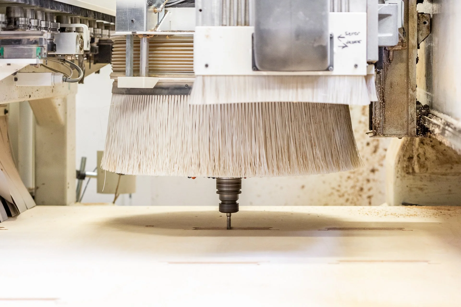 Machine industrielle utilisant une brosse pour couper ou polir du matériau, probablement du bois ou de la mousse, dans un environnement de fabrication.