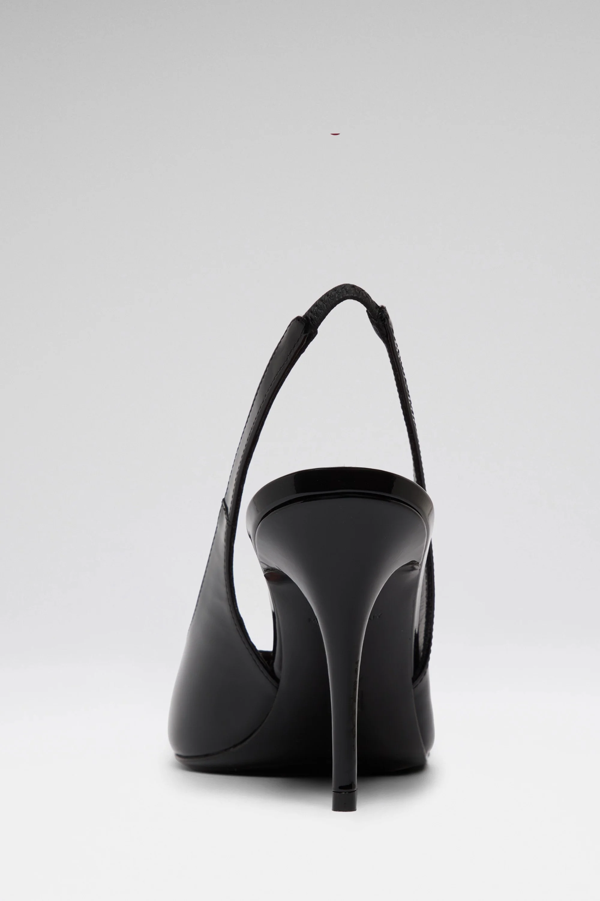 Une chaussure noire à talon aigu, vue de dos, contre un fond blanc clair.