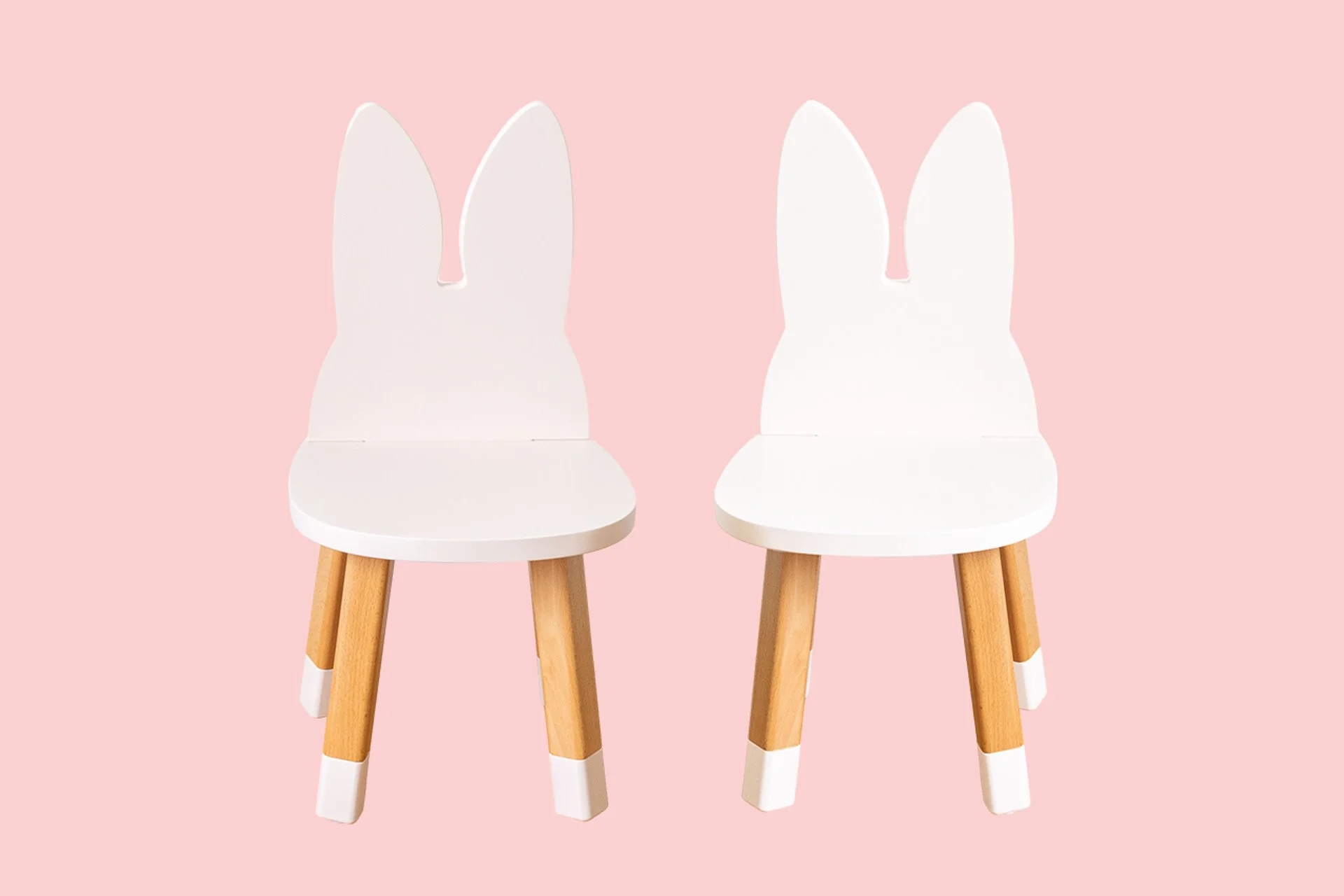 Deux chaises blanches avec jambes en bois, conçues pour ressembler à des lapins avec des oreilles en haut, sur un fond rose clair.