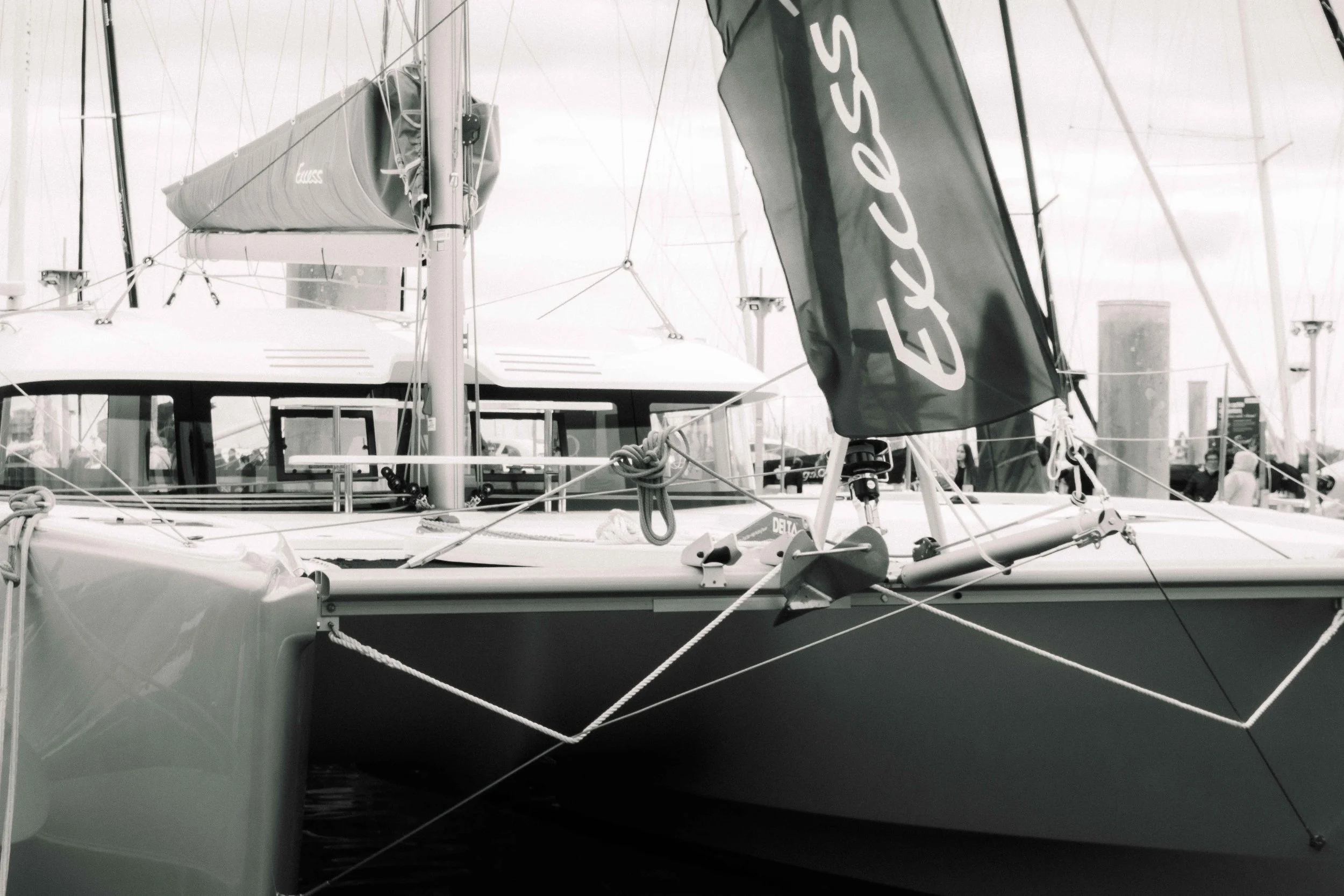 Voilier au port avec ses voiles pliées, des cordages et une coque visible, en noir et blanc.