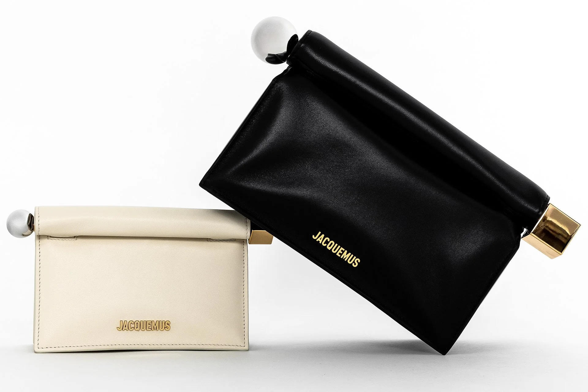 Deux sacs à main de la marque Jacquemus, un blanc et un noir, avec des détails en or, affichés sur fond blanc.