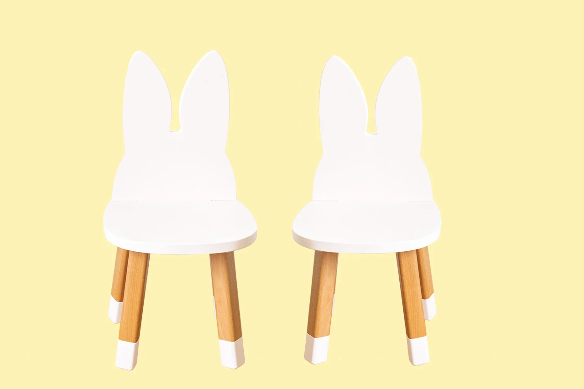 Deux chaises pour enfants avec un design de lapin, assises blanches, jambes en bois clair avec des extrémités blanches, sur fond jaune pâle.