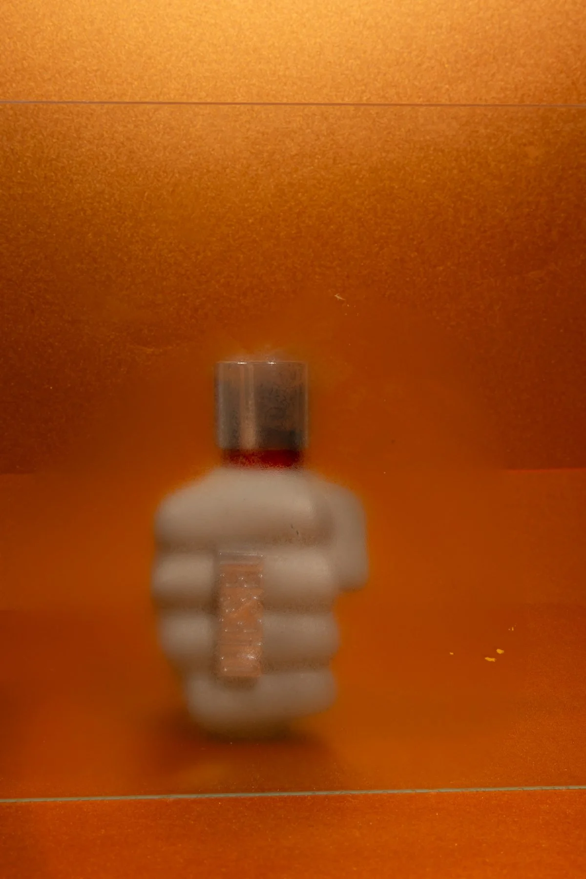 Une bouteille de parfum en forme de main, avec un fond marron orangé.