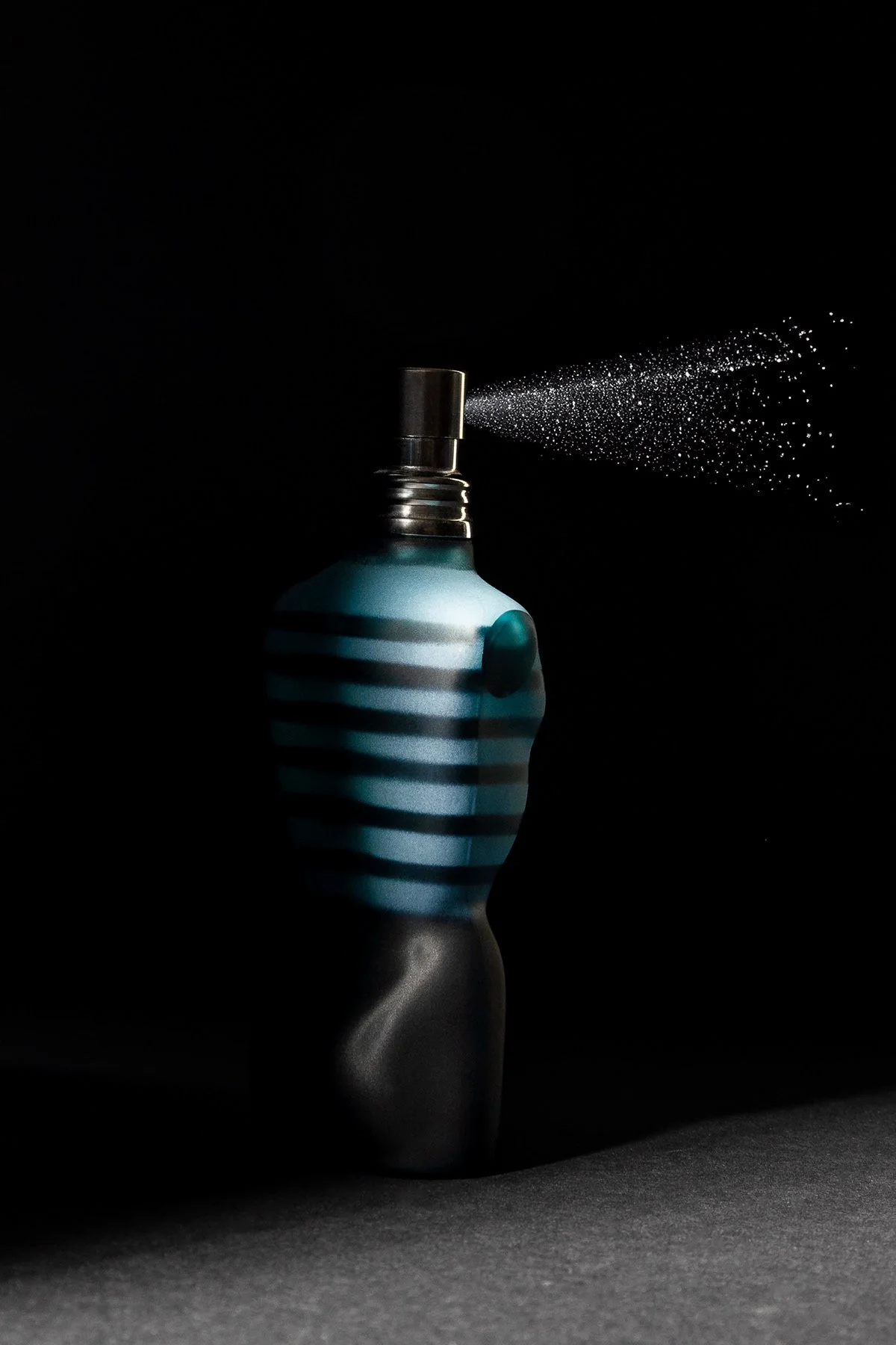 Un flacon de parfum bleu avec des rayures blanches, émettant une fine brume dans un environnement sombre.