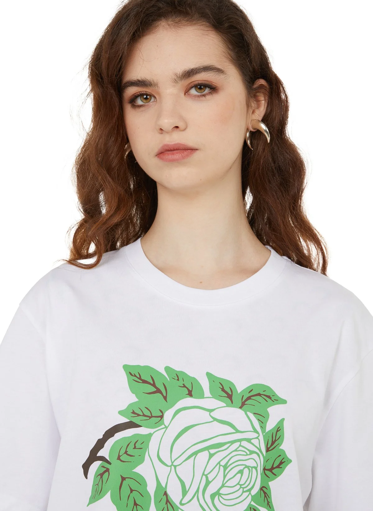 Une jeune femme avec des cheveux ondulés bruns porte un t-shirt blanc avec une illustration d'une rose verte.