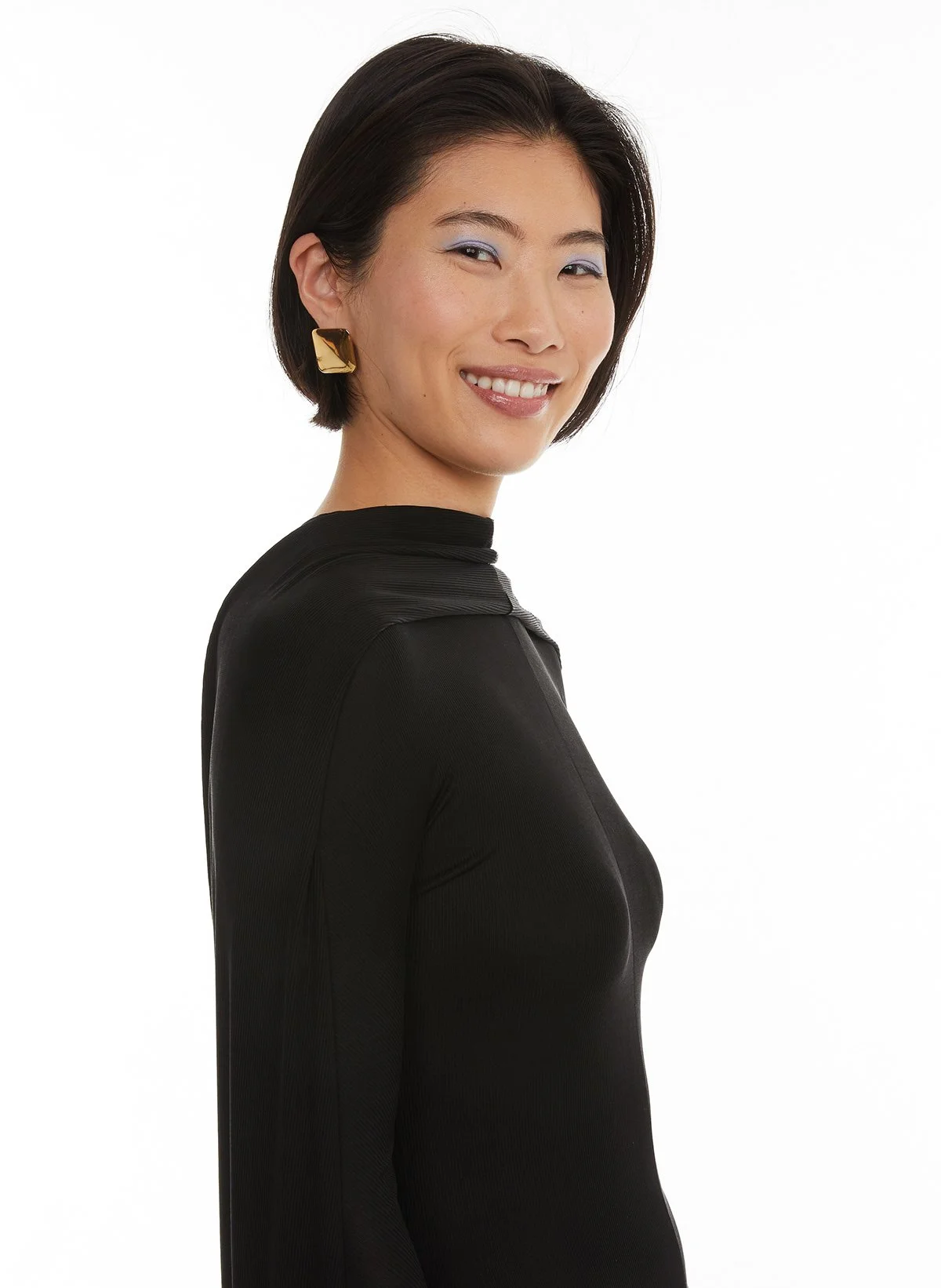 Portrait d'une femme souriante portant un vêtement noir et des boucles d'oreilles dorées, avec un fond blanc.