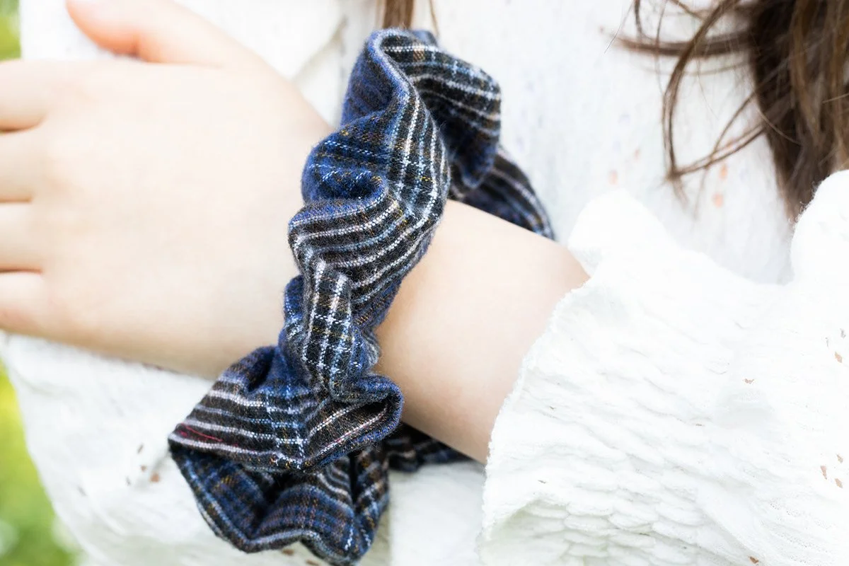 Poignet d'une personne avec un scrunchie en tissu à motif plaid, vêtue d'une chemise blanche