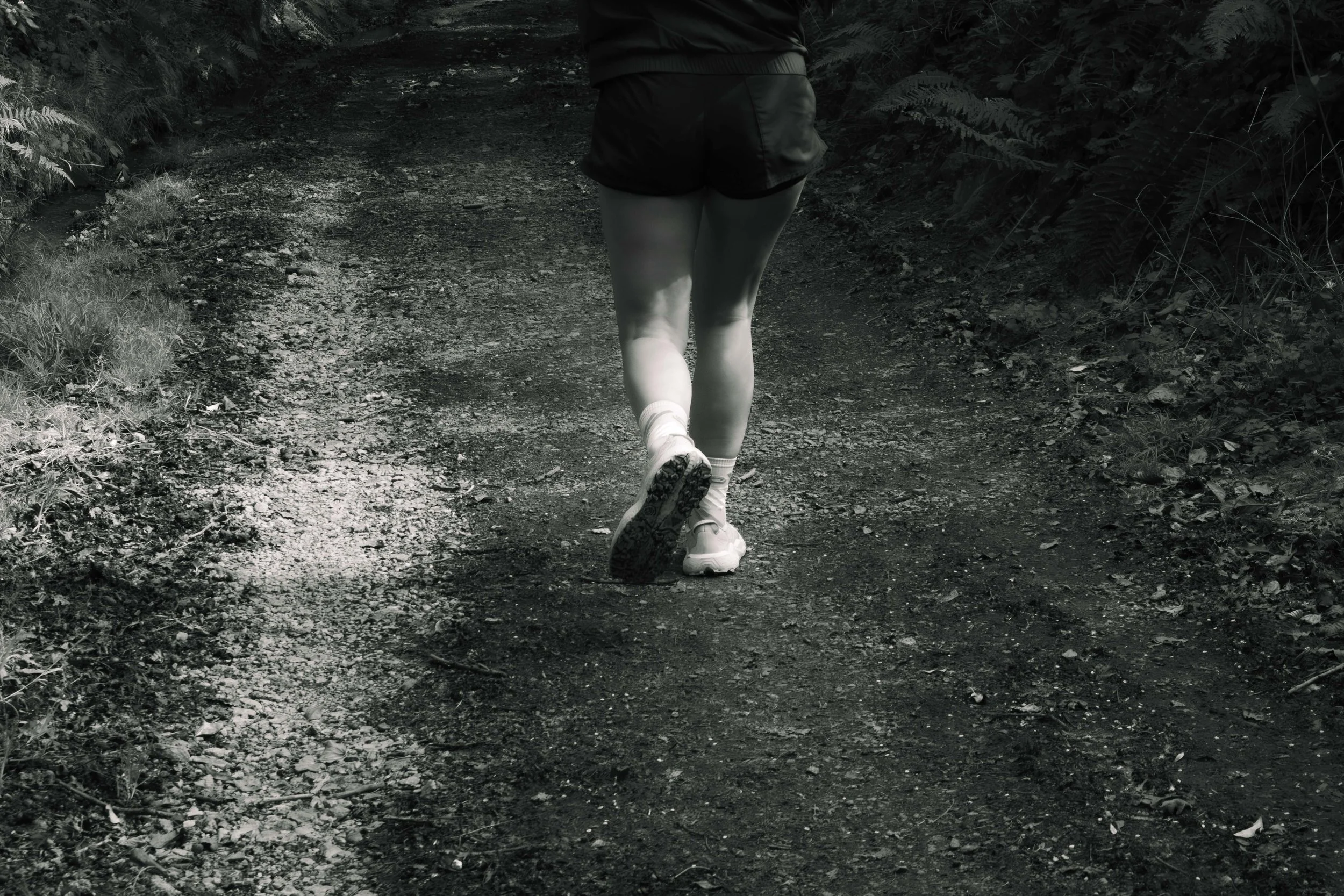 Une personne qui court sur un sentier forestier, vue de dos, en noir et blanc.